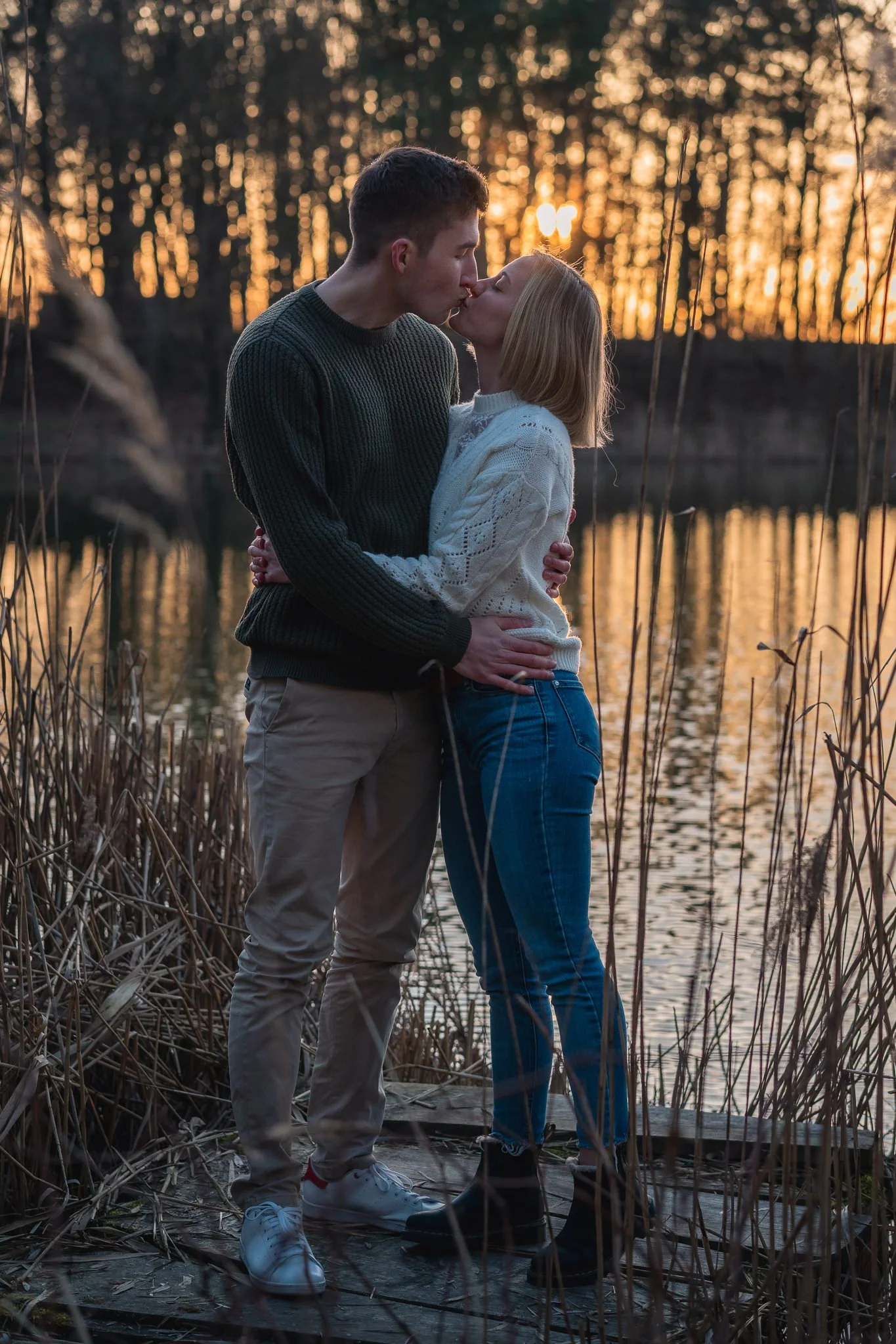 Ein verliebtes Paar küsst sich an einem See bei Sonnenuntergang, umgeben von Tall grass.