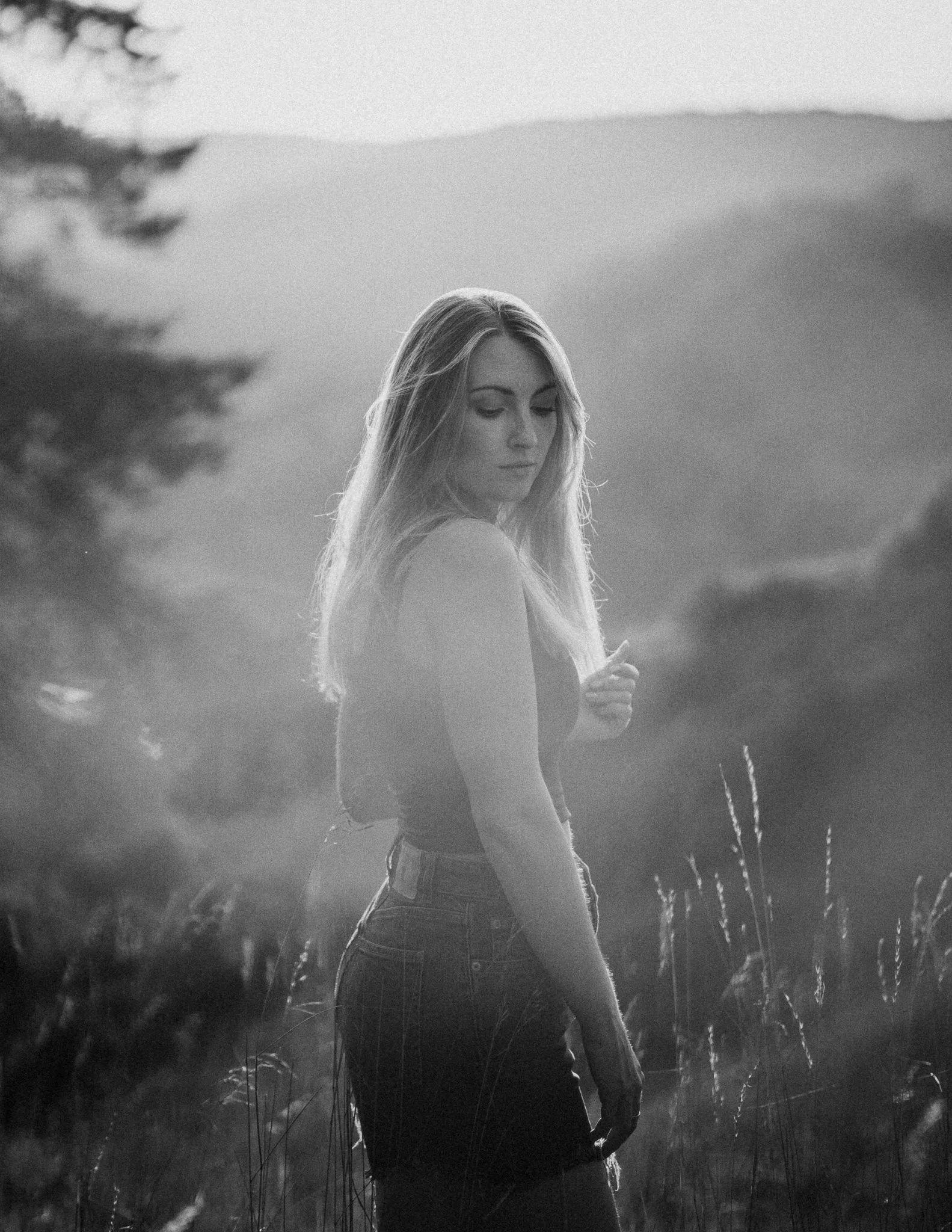 Schwarz-Weiß-Foto einer jungen Frau mit langem Haar, die in einem Feld steht und in die Ferne schaut.