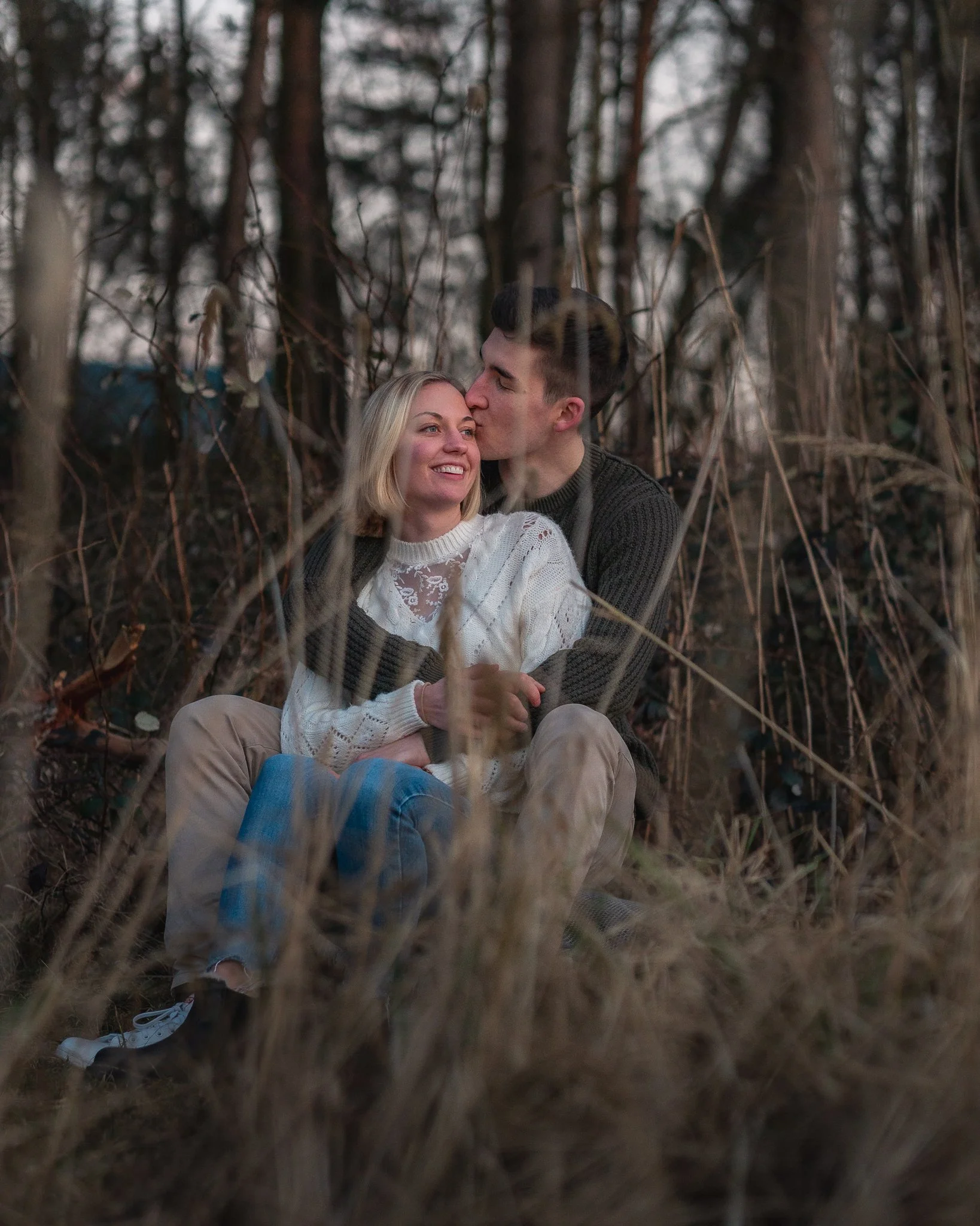 Ein Paar sitzt im Wald, er küsst sie auf die Wange, sie lächelt glücklich.