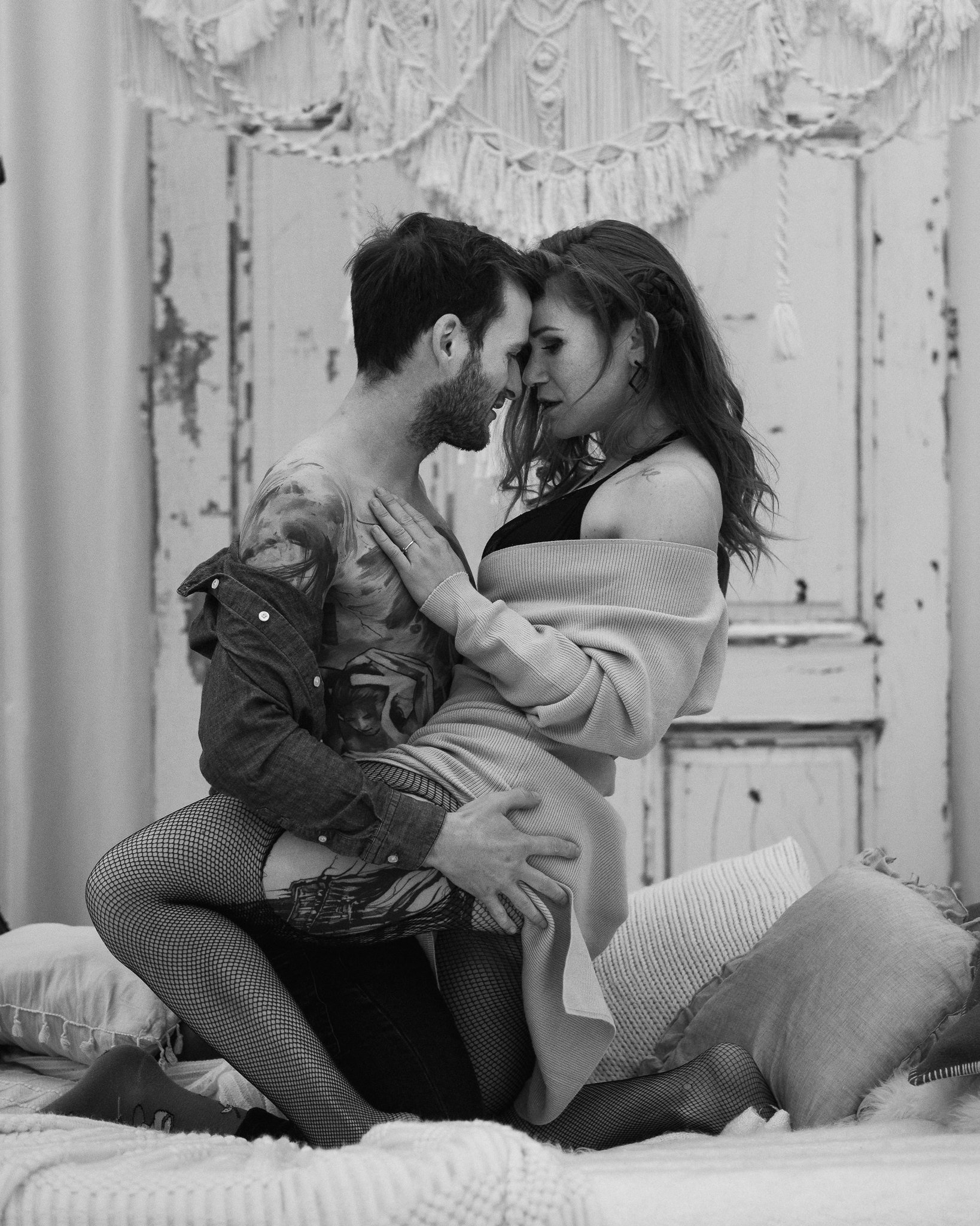 Ein Mann und eine Frau sitzen auf einem Bett und berühren ihre Stirnen, in einer intimen Pose.