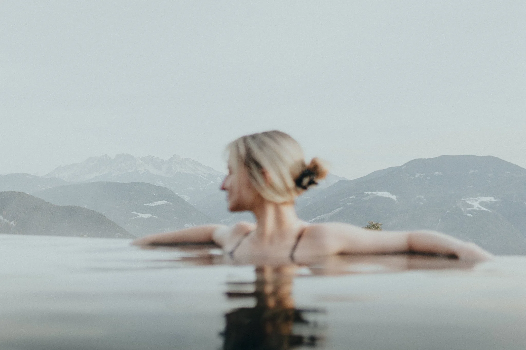 Frau entspannt im Wasser mit Berggipfeln im Hintergrund.