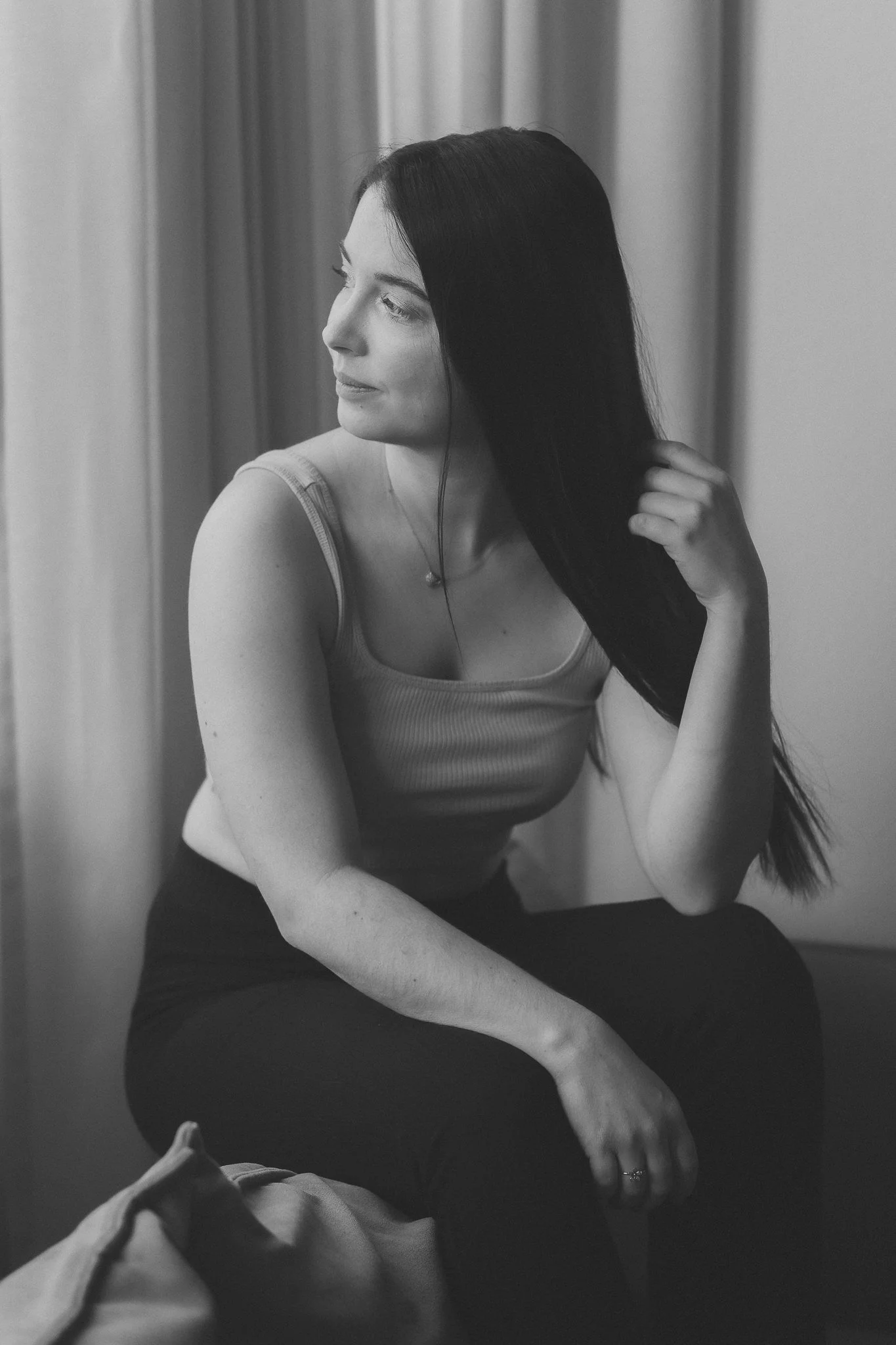 Schwarze und weiße Fotografie eines blondes Mädchens, das mit gekreuzten Beinen sitzt und in die Ferne schaut.