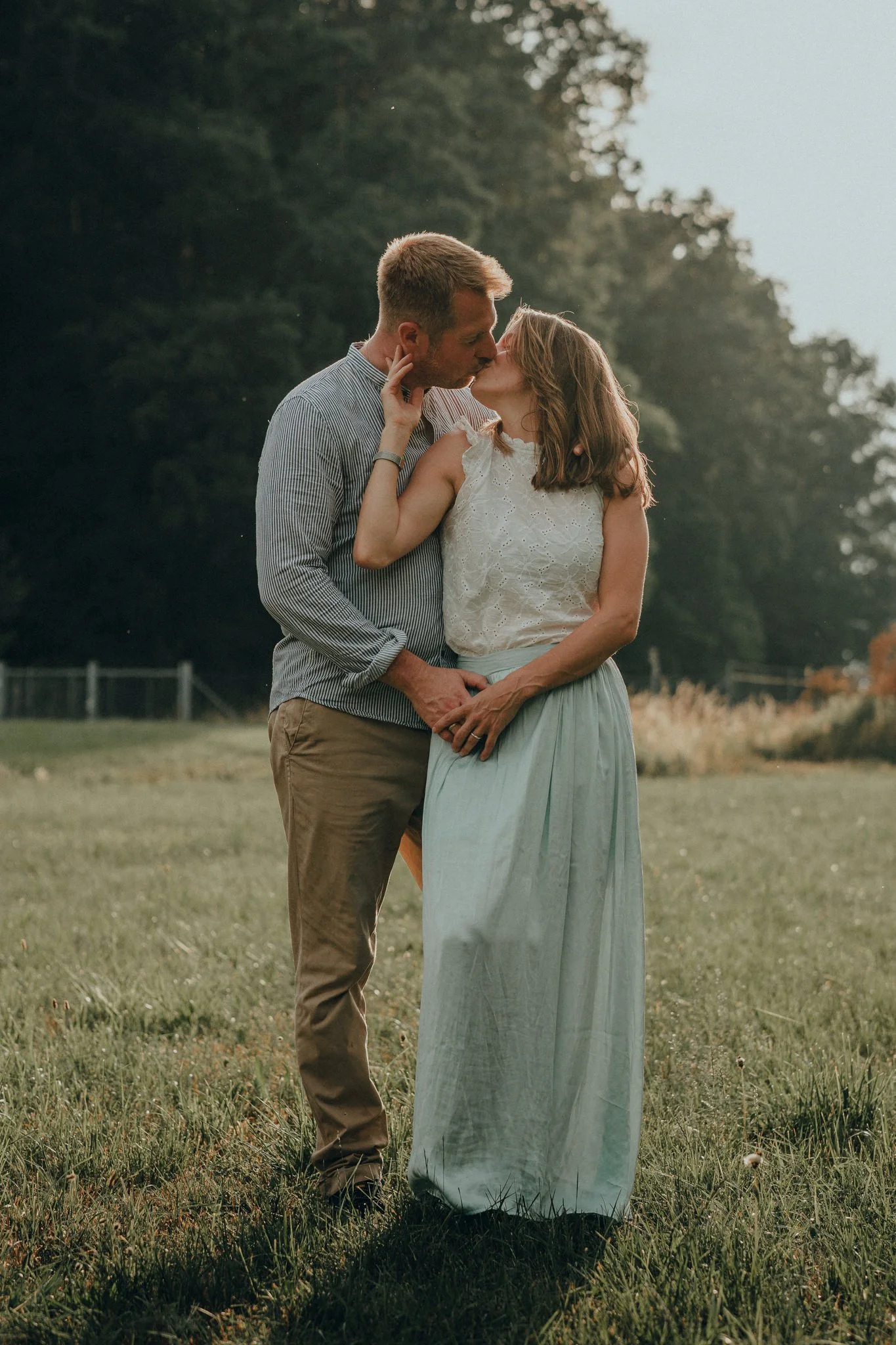 Ein verliebtes Paar küsst sich im Freien bei Sonnenuntergang, umgeben von Natur.
