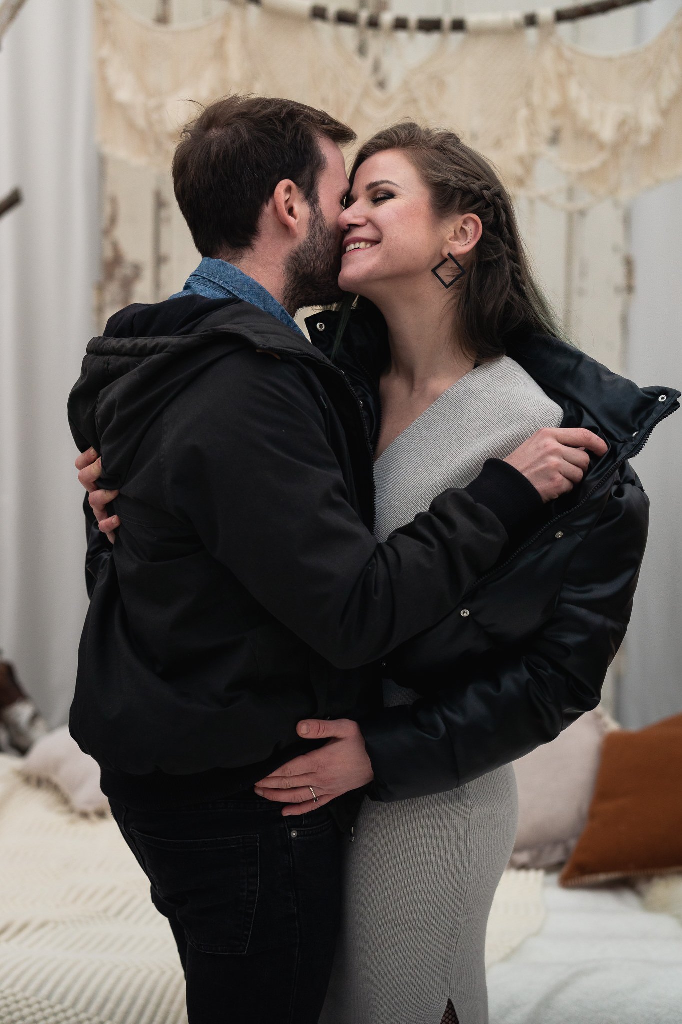 Ein Mann und eine Frau umarmen sich liebevoll in einem Raum mit dekorativer Wand im Hintergrund.