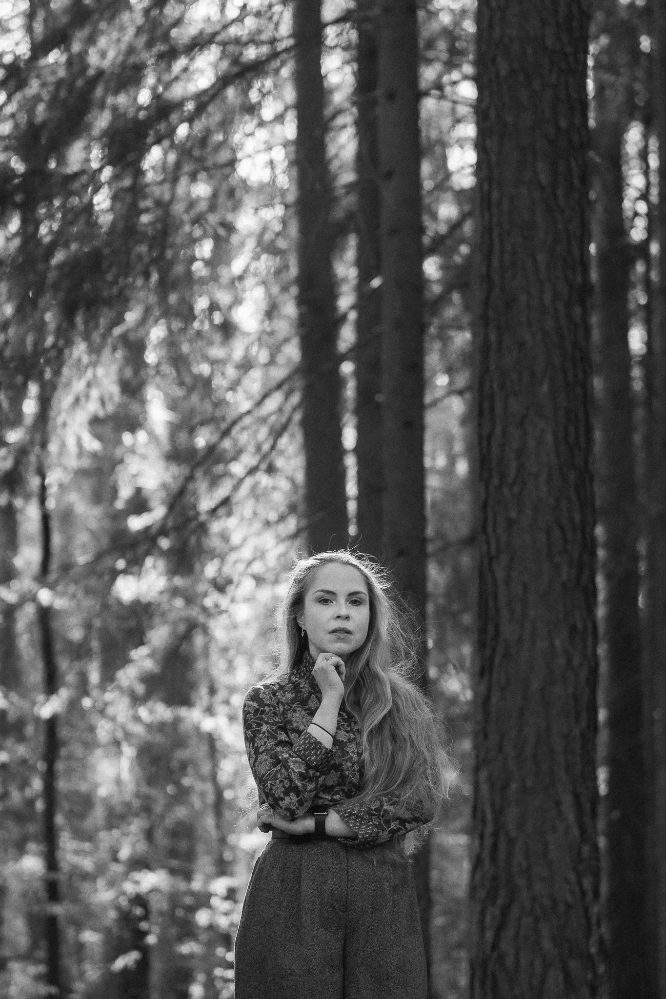 Schwarz-weiß-Foto einer Frau mit langen Haaren in einem Wald, trägt ein gestreiftes Langarmshirt und hohe Taille Hosen.