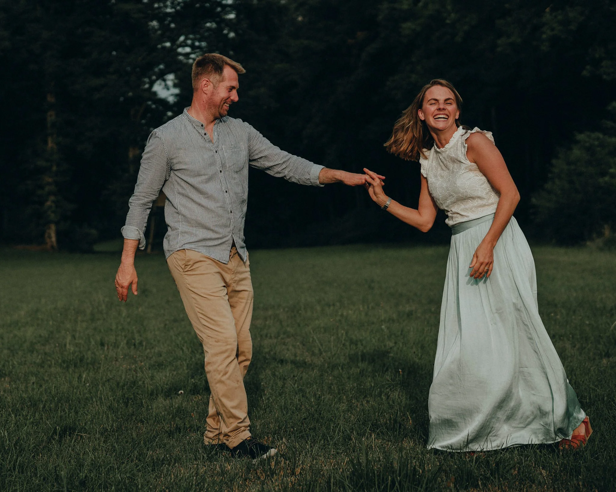 Ein Mann und eine Frau laufen lachend über eine grüne Wiese, der Mann hält die Hand der laufenden Frau.