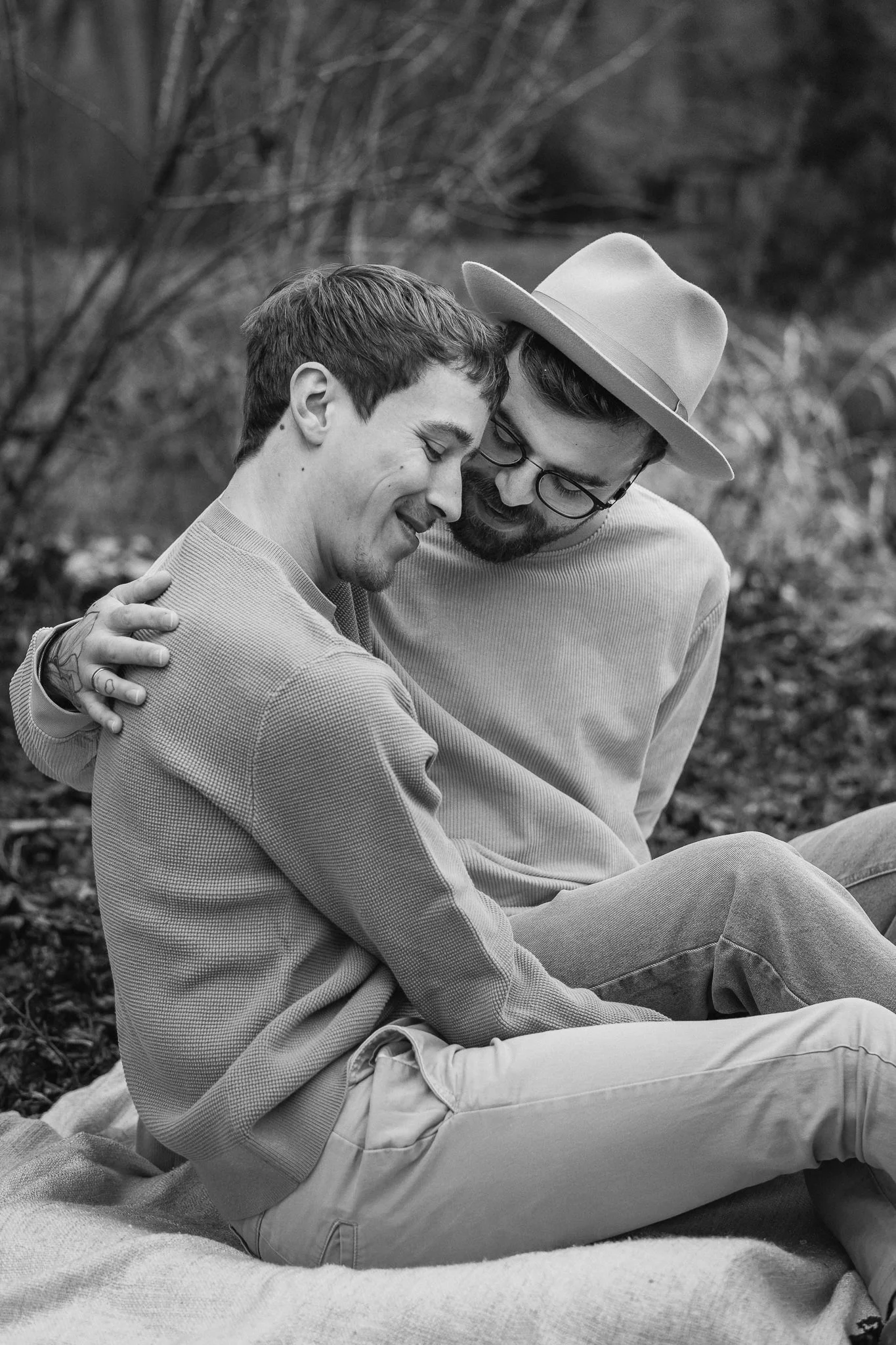 Zwei Männer sitzen im Freien, lächeln sich an und umarmen sich, während sie auf einem Tuch sitzen.