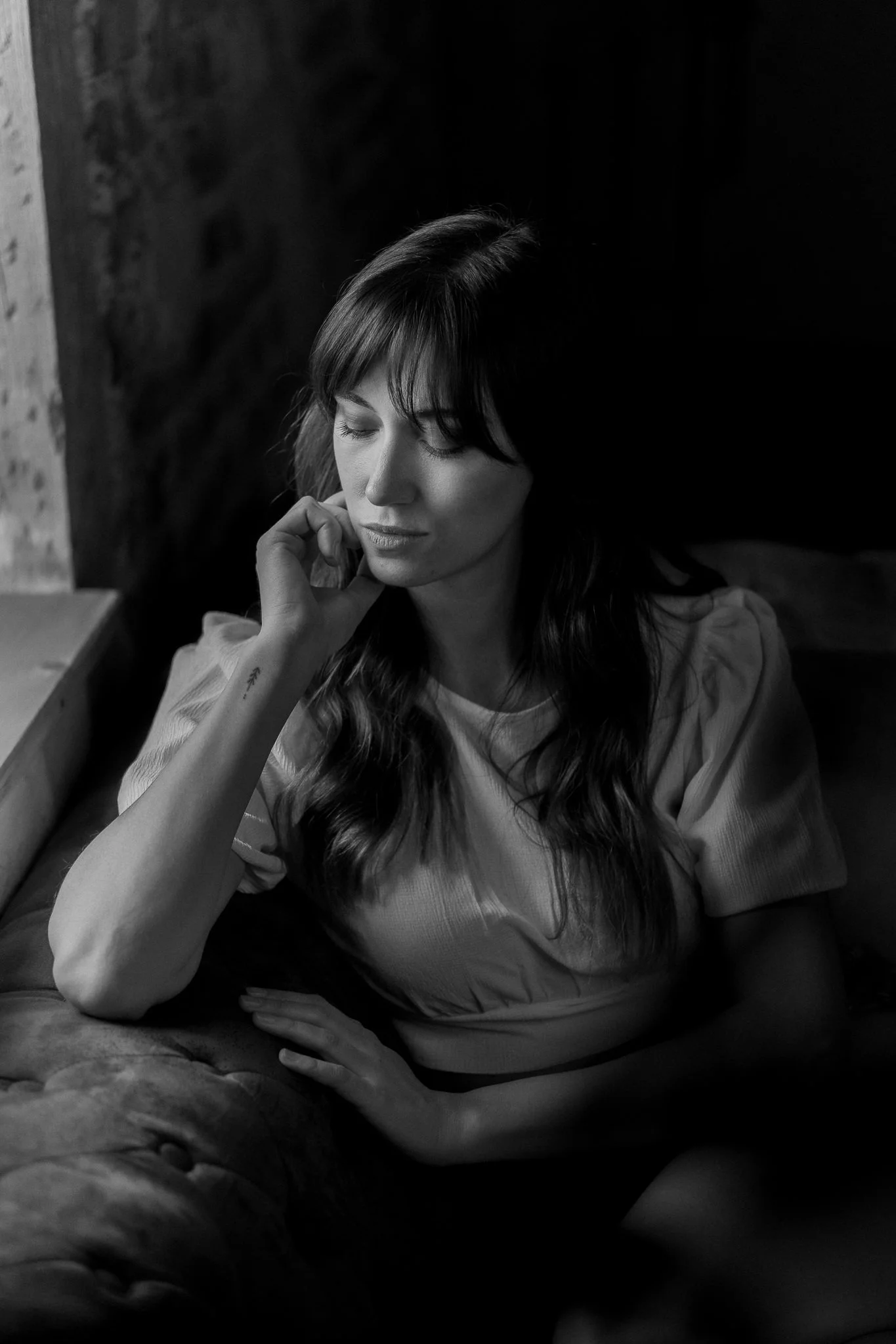 Schwarz-weiß-Foto einer Frau mit langen dunklen Haaren, die mit geschlossenen Augen auf einem Sofa sitzt, die Hand an ihrem Gesicht.