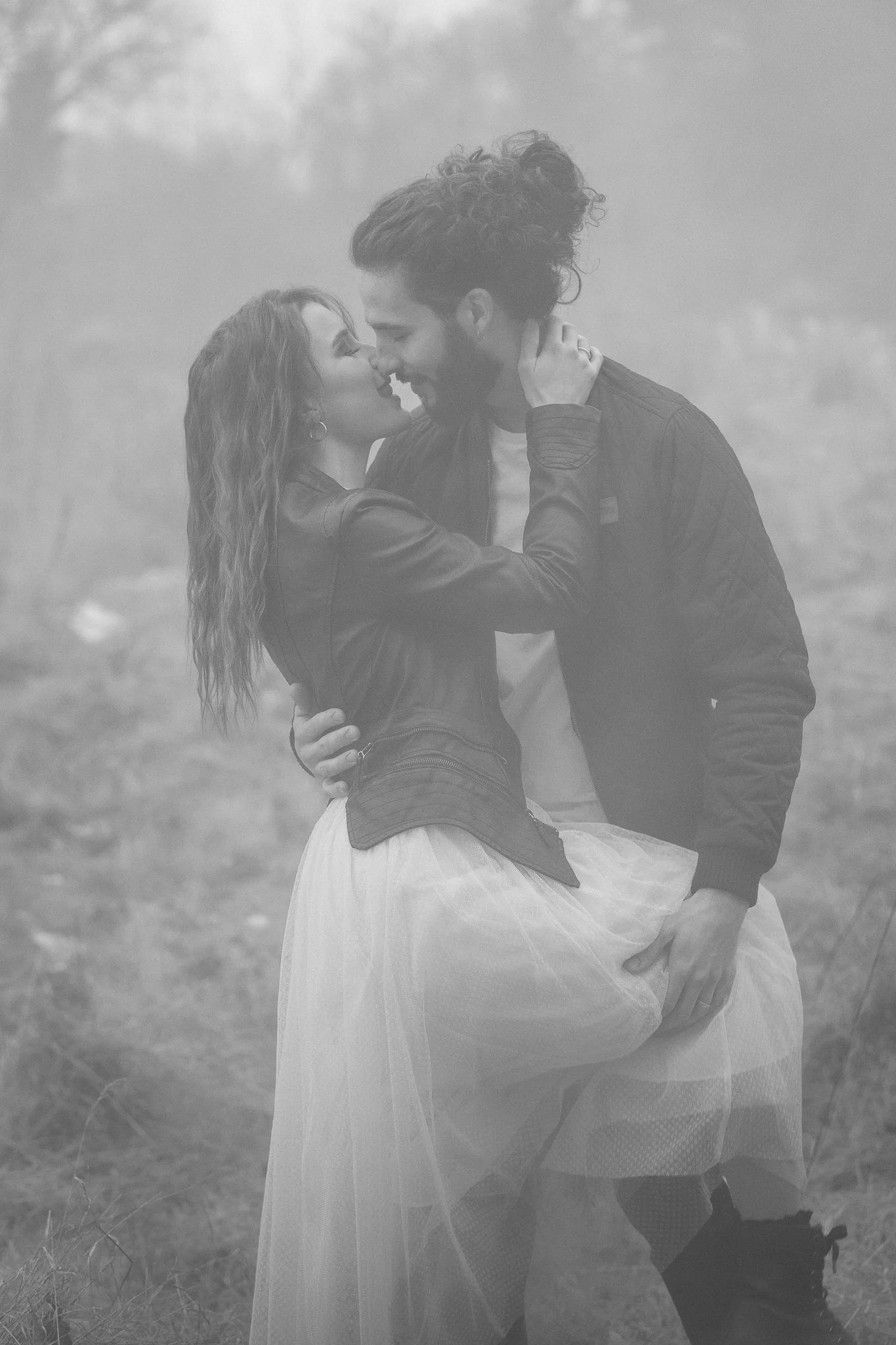 Ein verliebtes Paar umarmt sich im Freien bei Nebel, sie stehen sich sehr nah und lächeln sich liebevoll an.