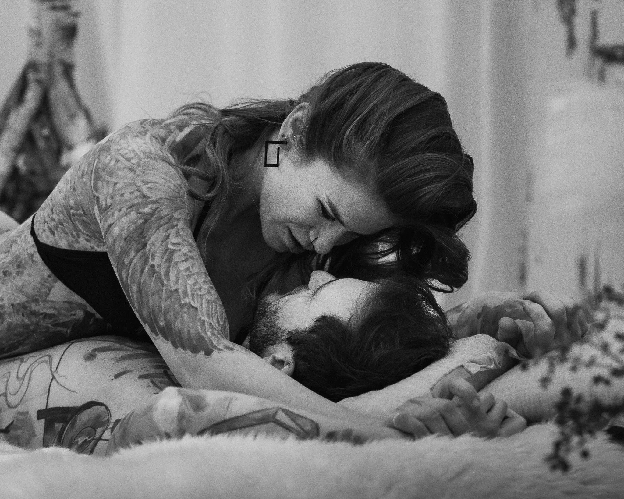 Ein Mann und eine Frau liegen auf einem Bett, die Frau beugt sich schützend über den Mann, sie schauen sich an.