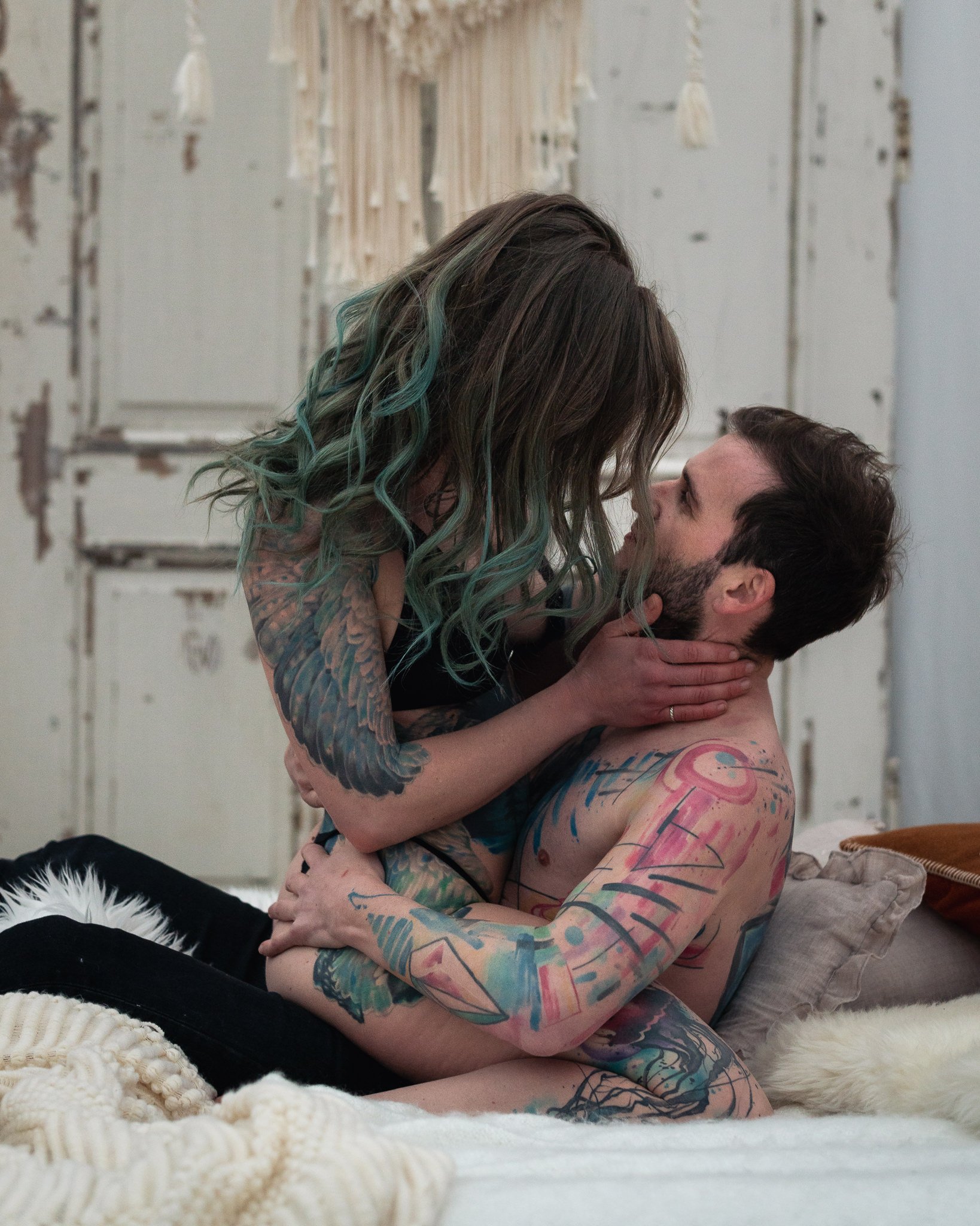 Ein tätowiertes Paar hat intimen Moment auf einem Bett in einem Raum mit weißen, abblätternden Wänden.