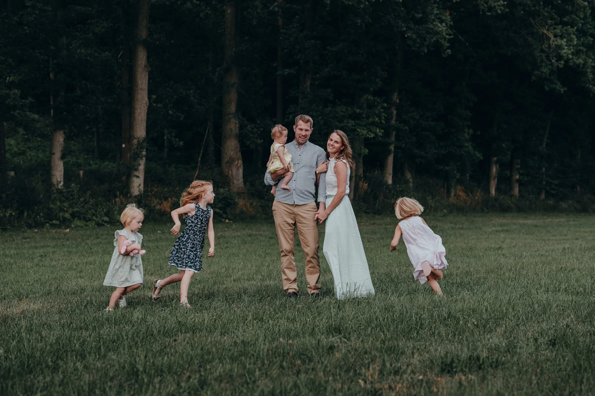 Eine Familie mit zwei Erwachsenen und vier Kindern, die im Grünen vor einem Wald spielen und lachen.