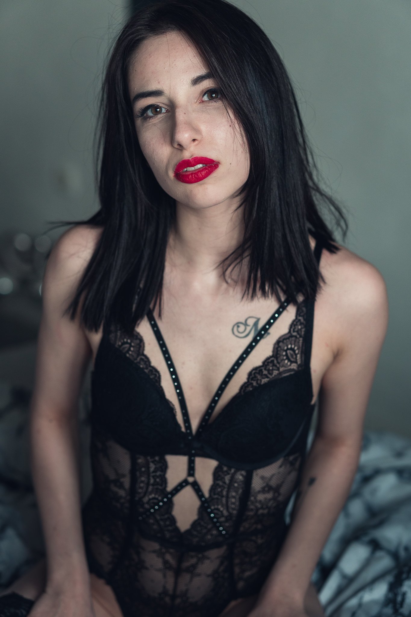 Junge Frau in dunkler, eleganter Spitze, blickt in die Kamera, mit roten Lippen und dunklem Haar.