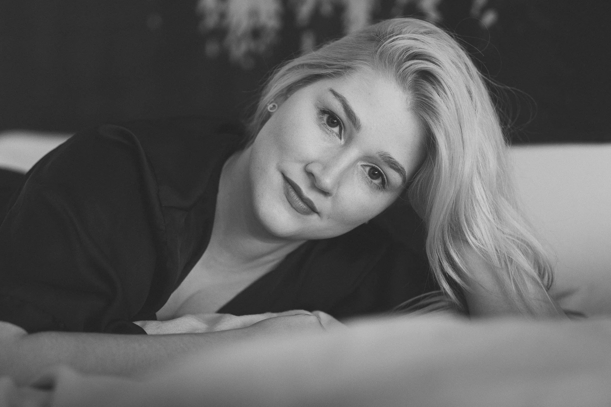 Schwarz-weiß-Foto einer jungen Frau mit blonden Haaren, die auf einem Bett liegt und die Kamera anlächelt.