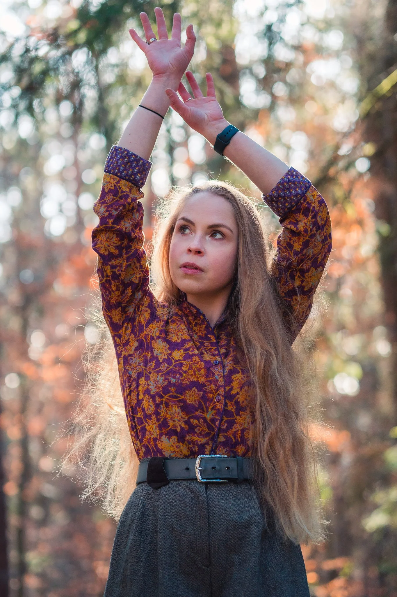 Junge Frau steht im Wald mit ausgebreiteten Armen und Blick nach oben.