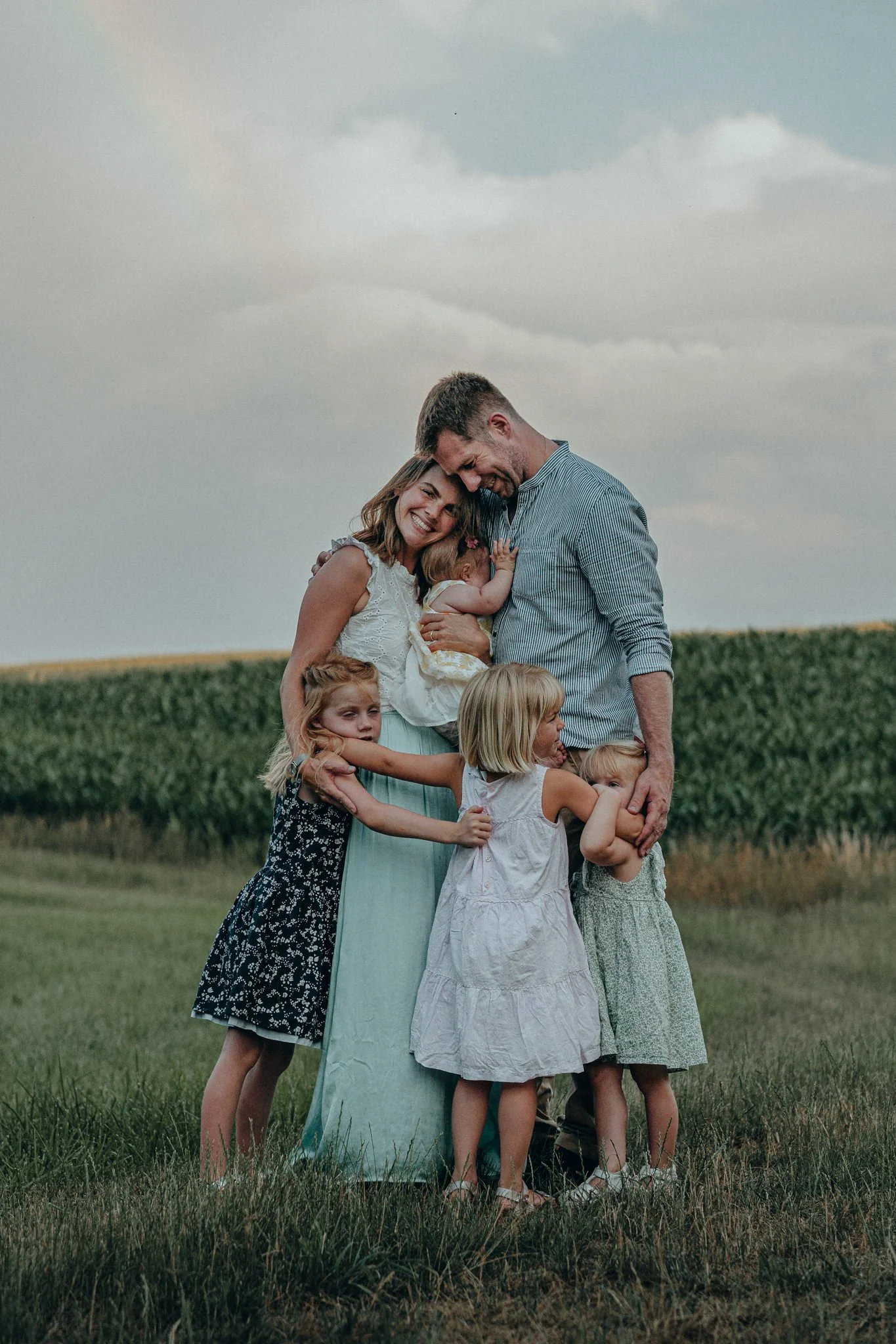 Familie mit Eltern und vier Kindern, einen kleinen Hund, in einem grünen Feld bei Sonnenuntergang, lachend und umarmend.