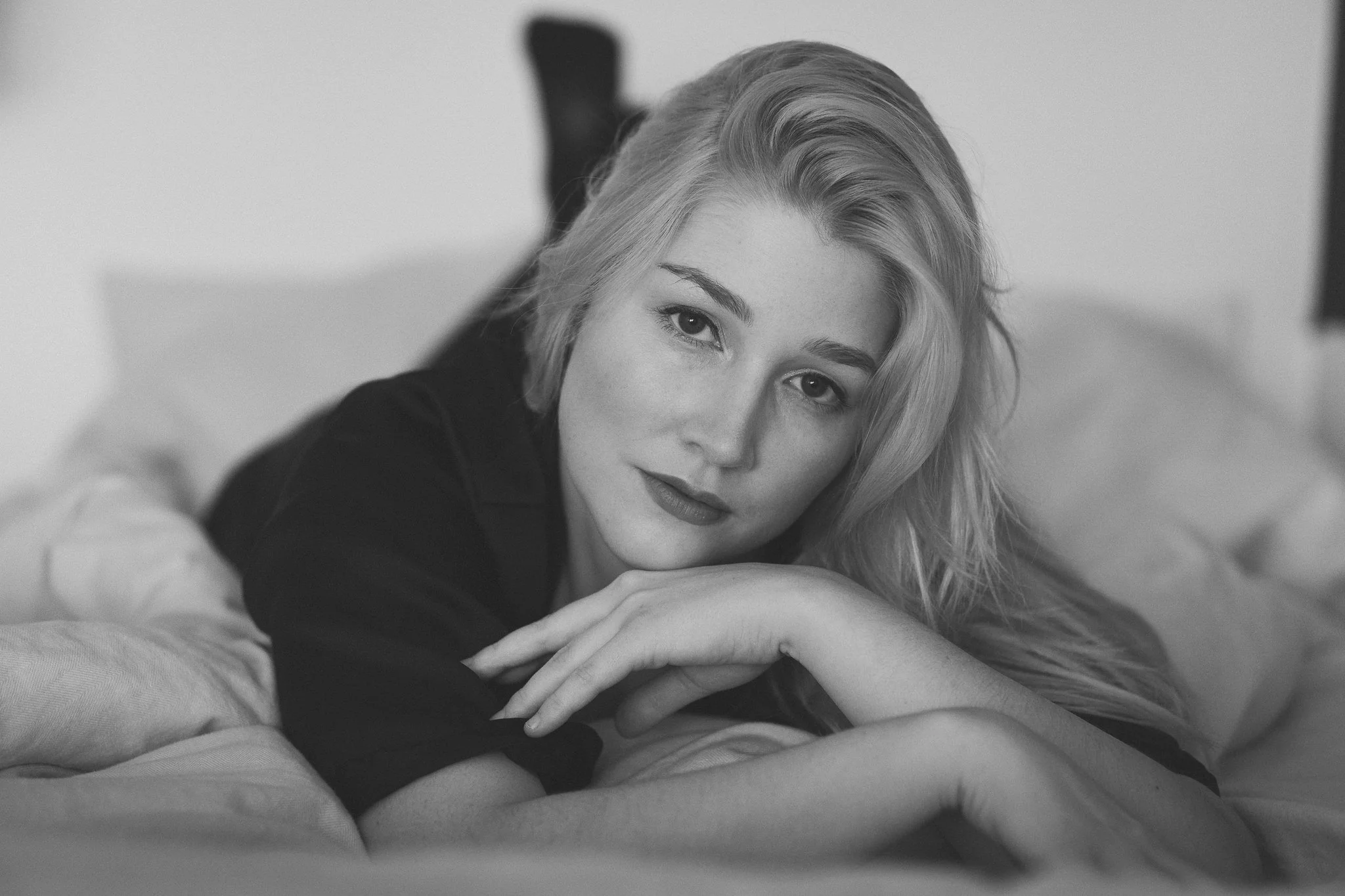 Schwarz-Weiß-Fotografie eines liegenden Mädchens mit offenen Haaren, liegend auf einem Bett, schaut in die Kamera.