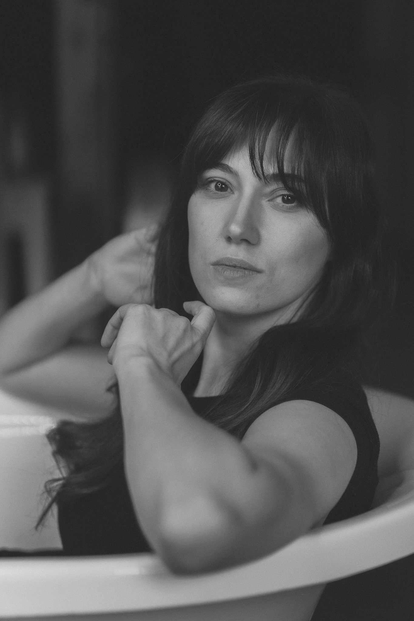 Schwarz-weiß-Fotografie einer Frau mit dunklen Haaren, die in einen Spiegel schaut und eine nachdenkliche Pose einnimmt.