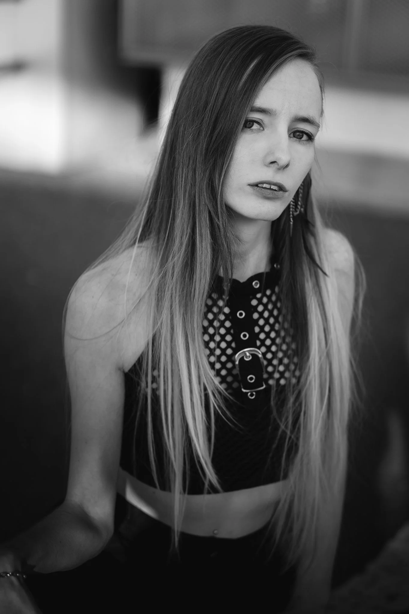 Schwarz-weiß-Foto eines jungen Mädchens mit langen, glatten Haaren, das an einem Tisch sitzt und direkt in die Kamera blickt.