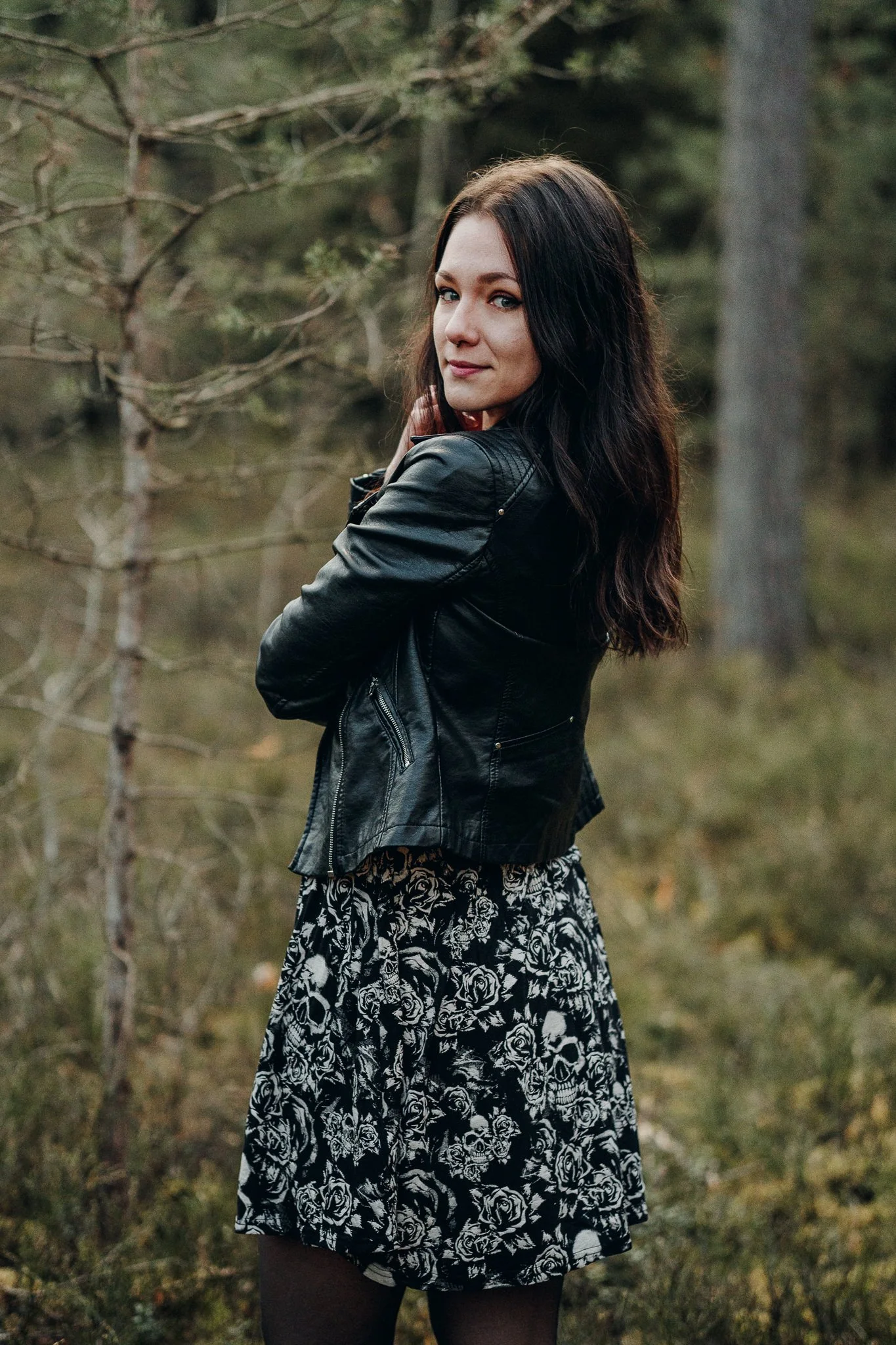 Junge Frau mit schwarzen Haaren, schwarzer Lederjacke und Kleid mit Totenköpfen und Rosen, im Wald.