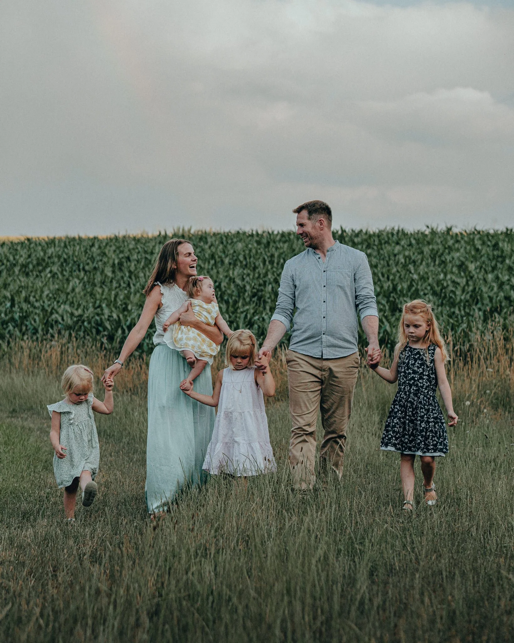 Familie mit Eltern und vier Kindern beim Spaziergang auf einer Wiese neben einem Getreidefeld im Freien.
