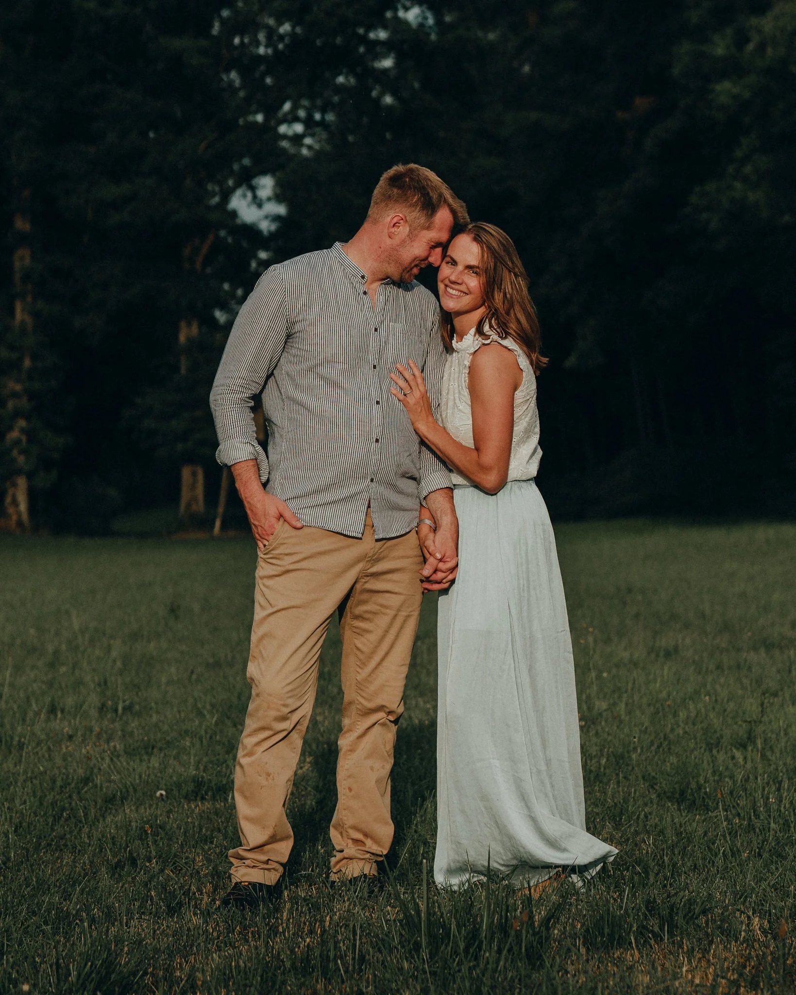 Ein Paar, das auf einer Wiese abends liebevoll Zärtlichkeiten austauscht, im Hintergrund Bäume.