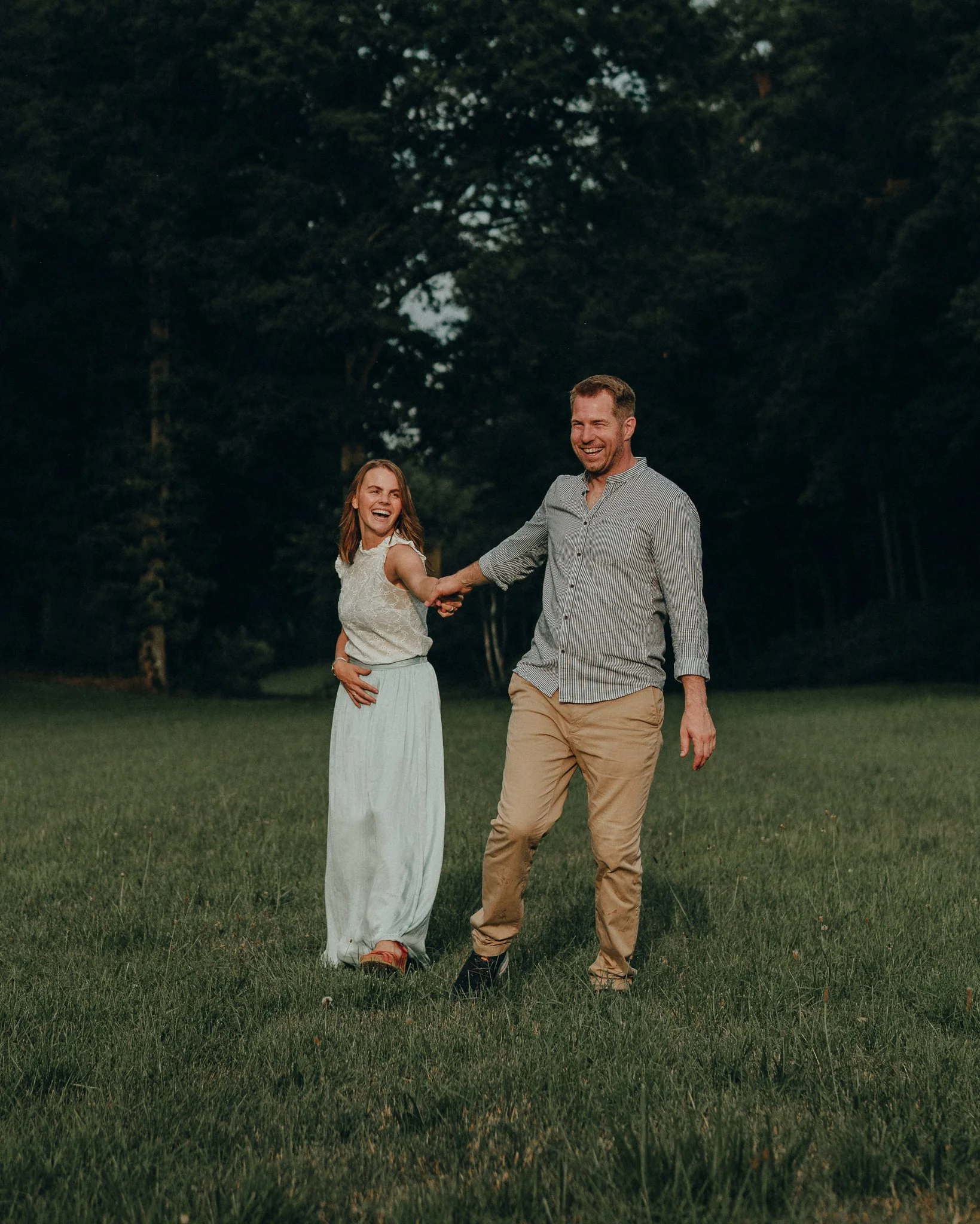 Ein lachendes Paar läuft grünem Feld bei Sonnenuntergang, Hand in Hand.