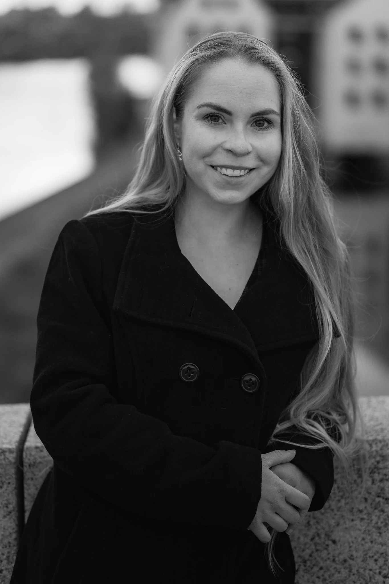 Junge Frau mit langen, lockigen Haaren in dunklem Mantel, lächelnd, im Freien, schwarz-weiß, porträtiert