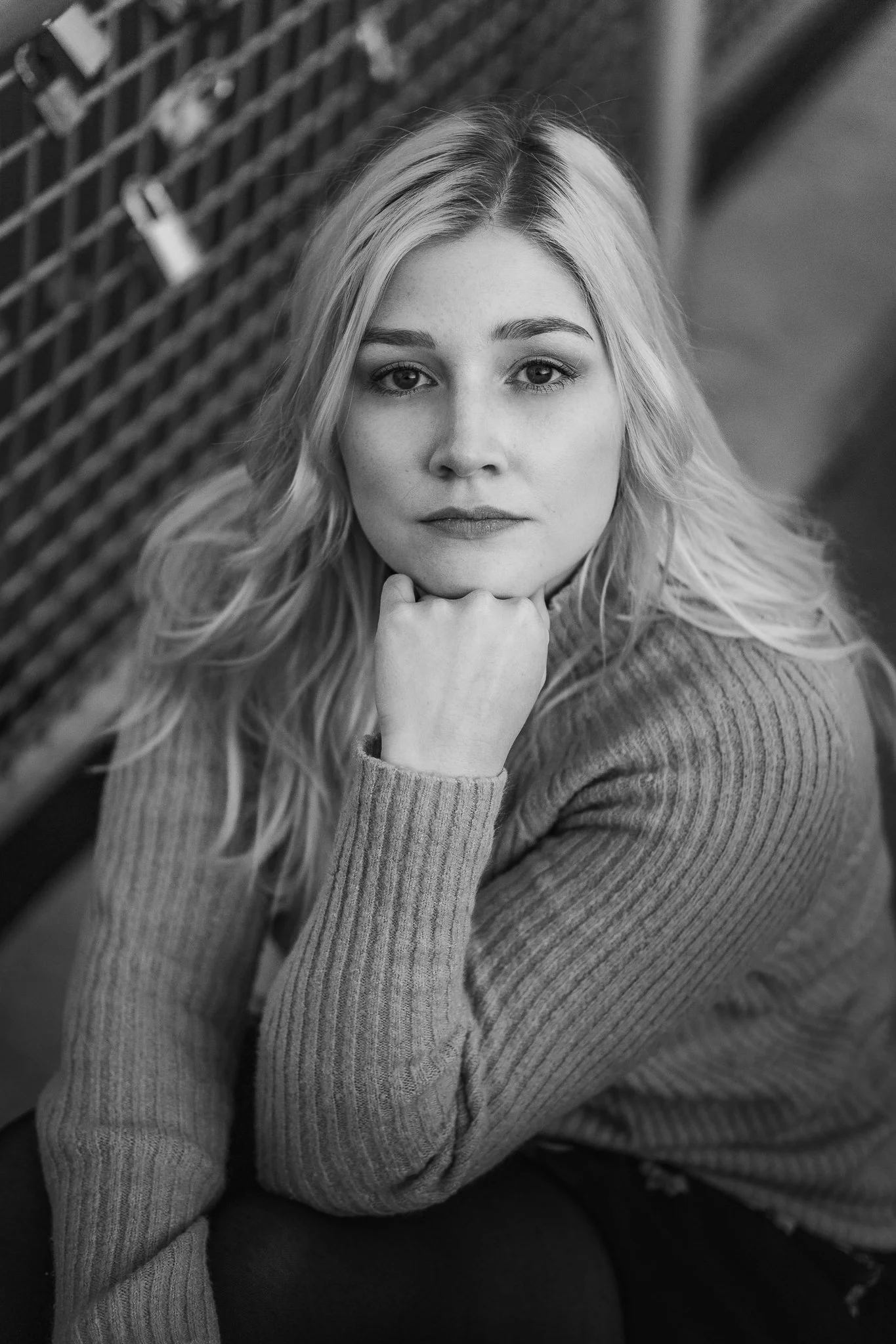 Schwarz-Weiß-Fotografie eines jungen Frauenporträts. Die Frau hat lange, gewellte Haare und trägt einen gestreiften Pullover. Sie schaut direkt in die Kamera mit einem nachdenklichen Ausdruck, ihre rechte Hand stützt ihr Kinn ab.