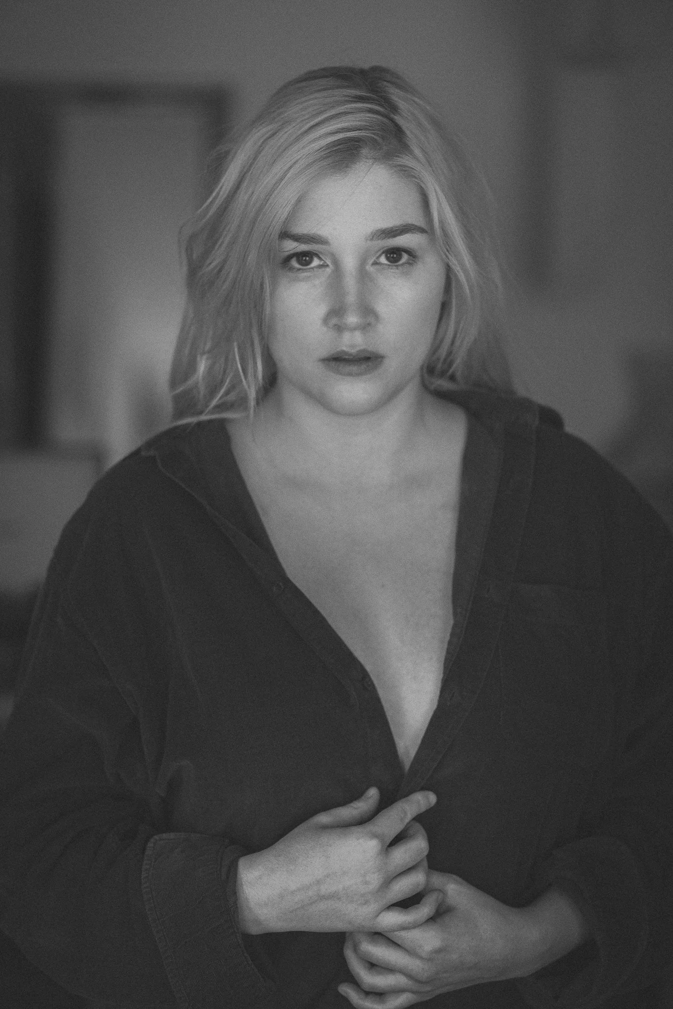 Schwarz-weiß-Foto eines jungen Frauenporträts, die direkt in die Kamera schaut, mit offenem schwarzen Hemd, zurückhaltendem Ausdruck und verlaufenem Haar.