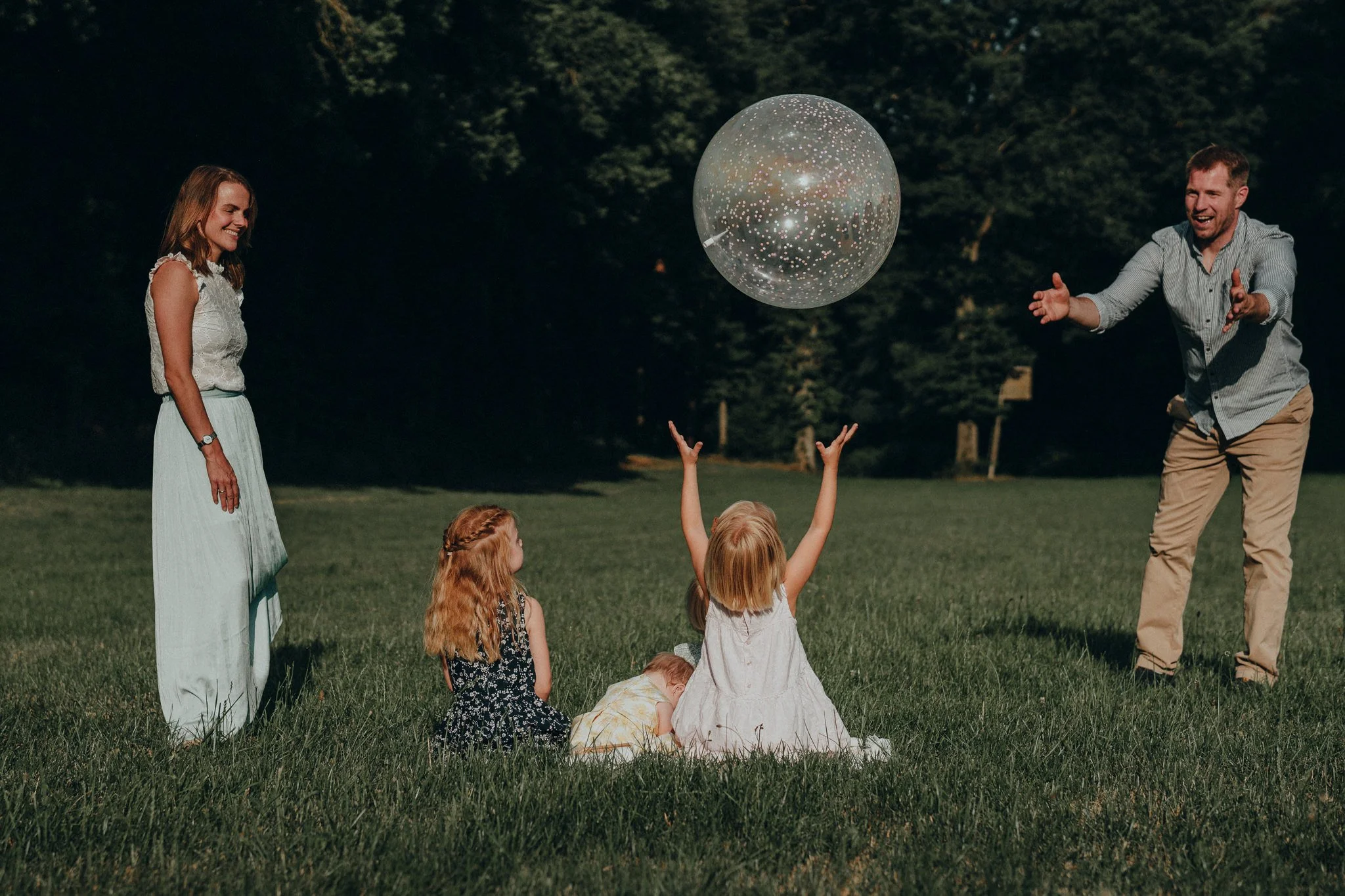 Familie mit drei Kindern spielt mit einem großen Ball im Park während des Sonnenuntergangs.