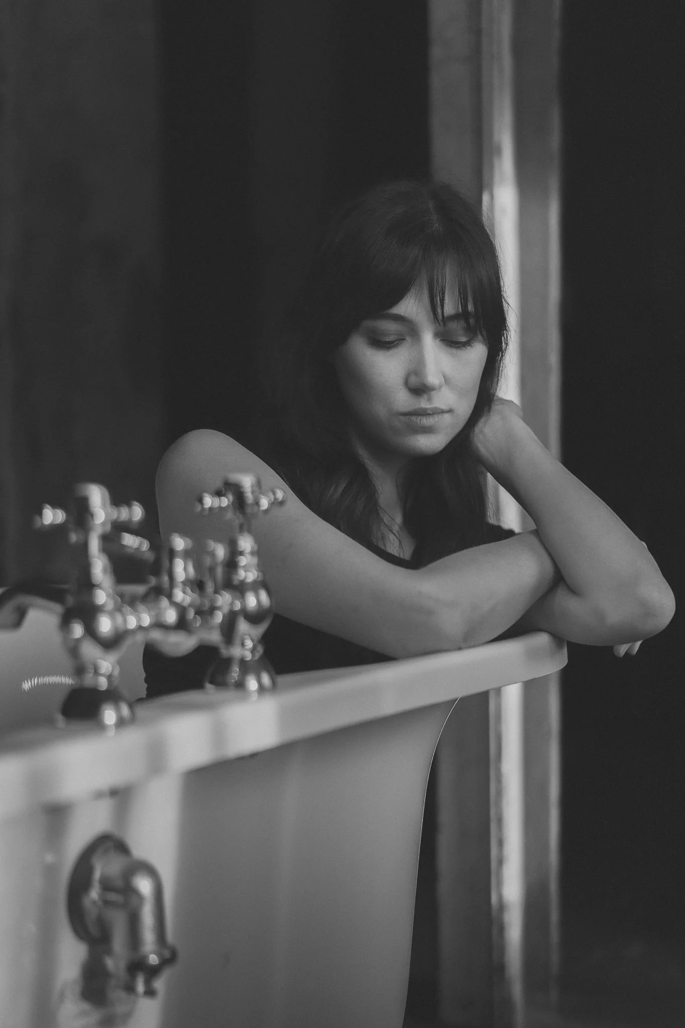 Schwarz-Weiß-Foto einer Frau mit dunklen Haaren, die an der Spüle lehnt, mit einem nachdenklichen Ausdruck.