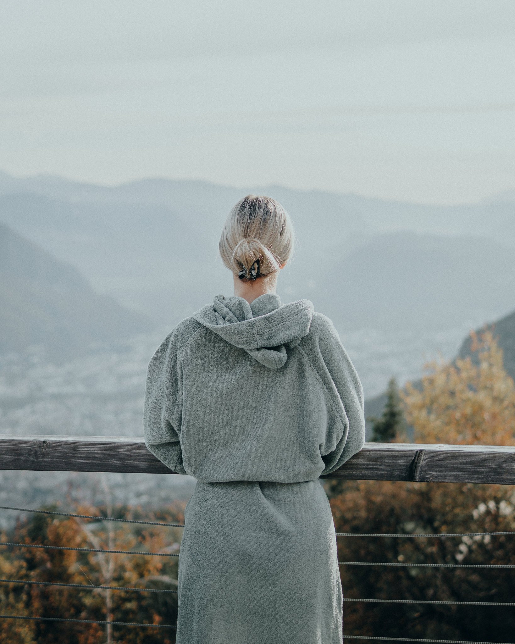 Eine Frau mit grauem Hoodie und Rock schaut auf eine Berglandschaft.