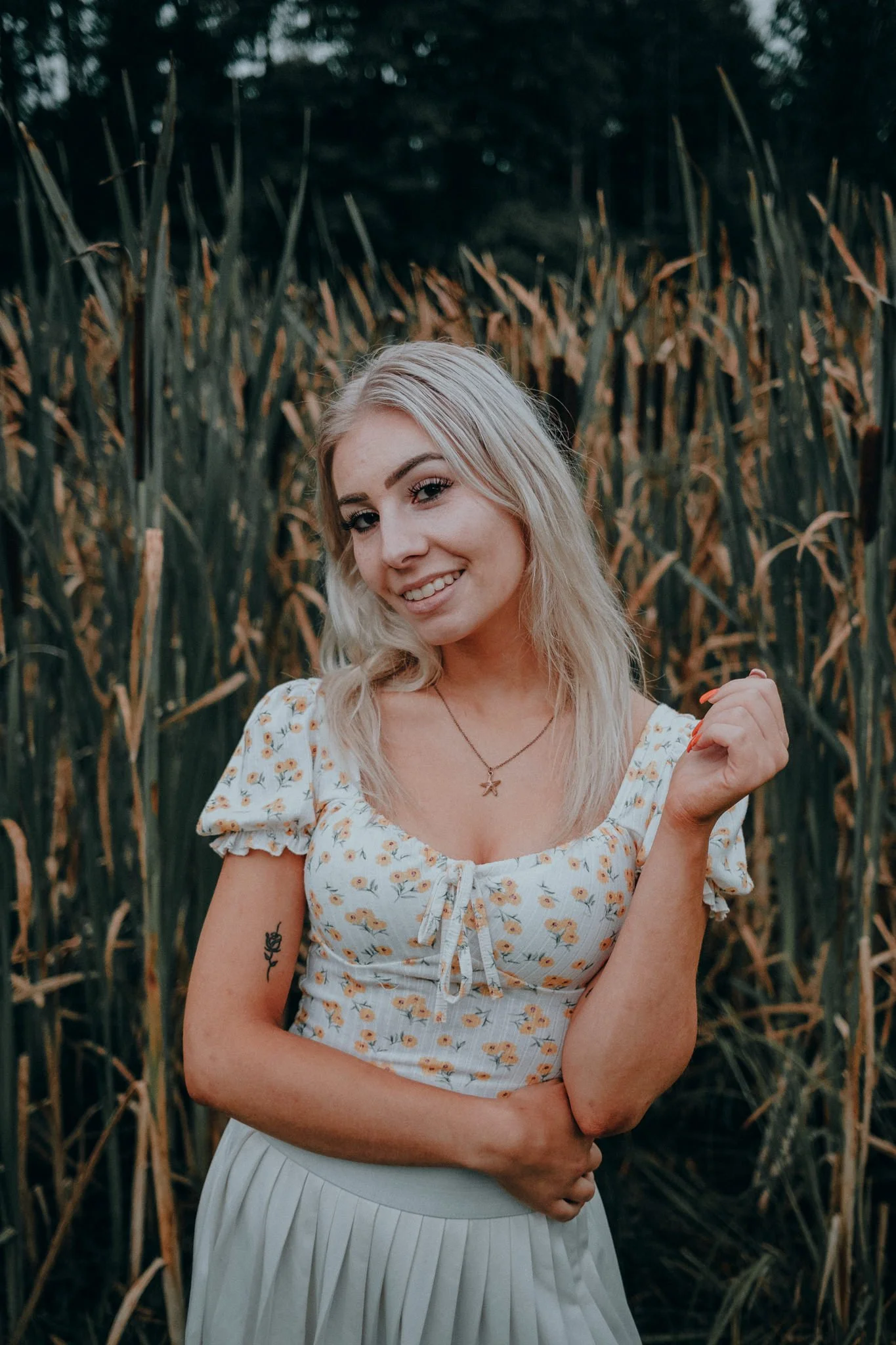 Eine lachende junge Frau mit blonden, lockigen Haaren steht vor einem Maisfeld.