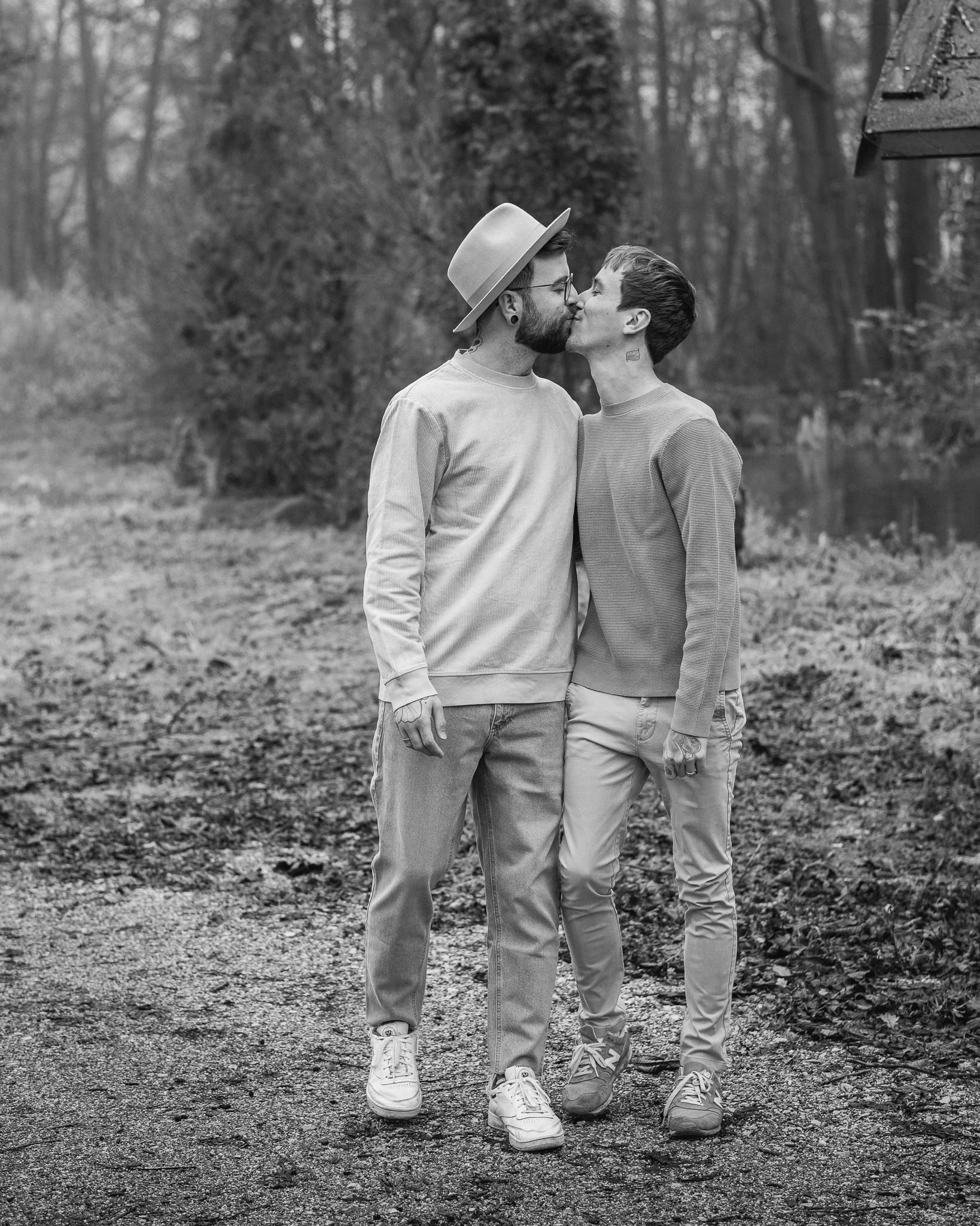 Zwei Menschen küssen sich im Freien, umgeben von Bäumen, in einer natürlichen Umgebung.