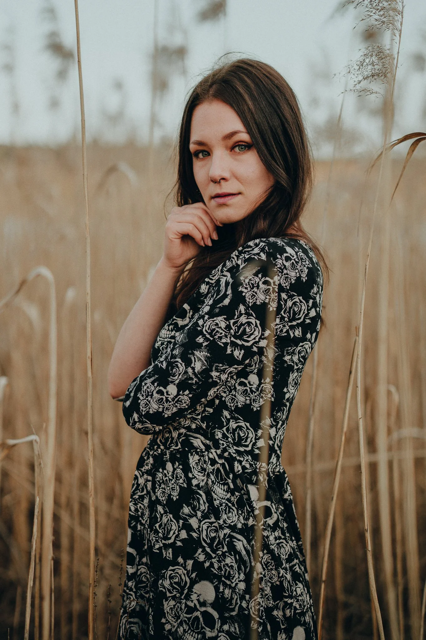 Jugendliche Frau mit dunklen Haaren und Tierkreis-Tattoo, die in einem Feld mit hohen Kürbispflanzen steht.
