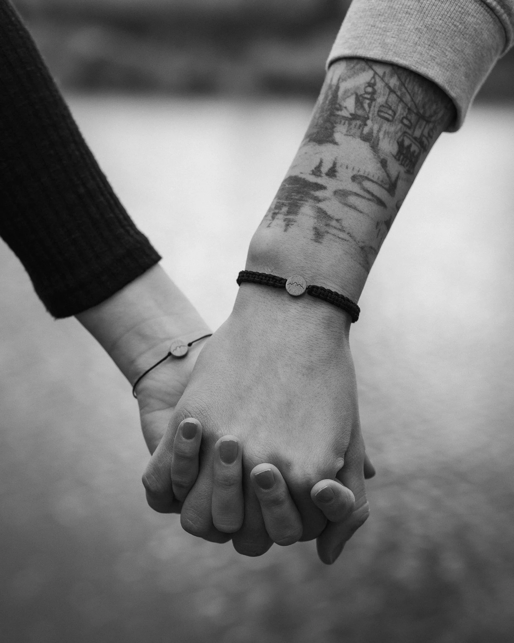 Zwei Menschen halten sich an den Händen, einer trägt eine Tätowierung am Arm und eine Armbanduhr, während der andere eine einfache Armbanduhr trägt.