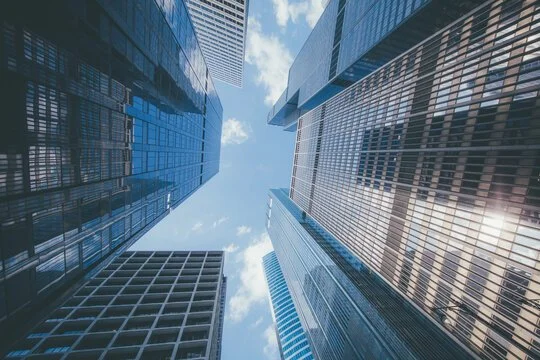 View looking up at tall glass skyscrapers in a city with blue skies and clouds.