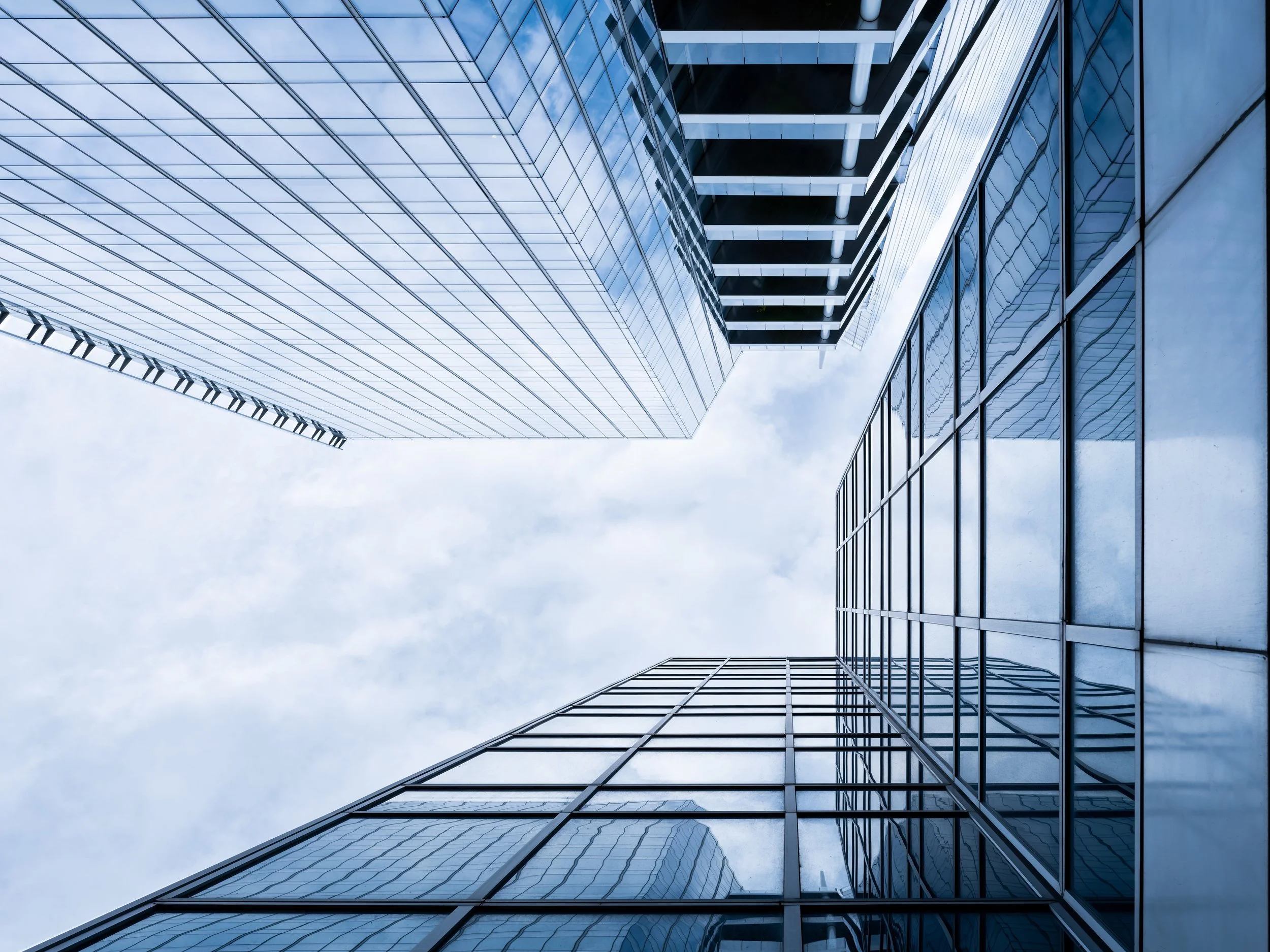 Tall modern glass building with reflective windows, viewed from below against cloudy sky.