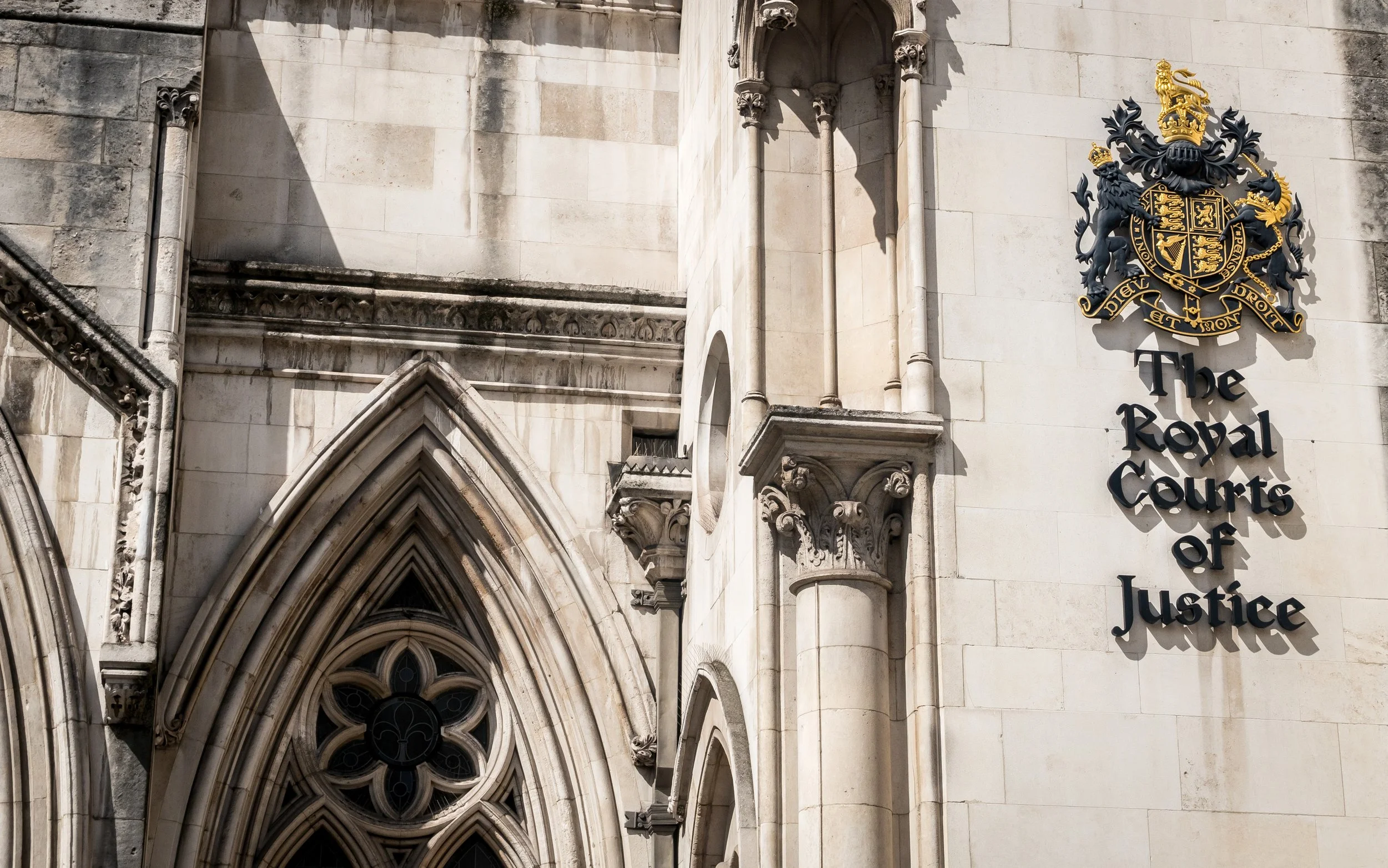 The exterior of a historic courthouse with gothic architecture, including decorative stonework, arched windows, and a crest with a lion and a crown on the wall that reads "The Royal Courts of Justice."