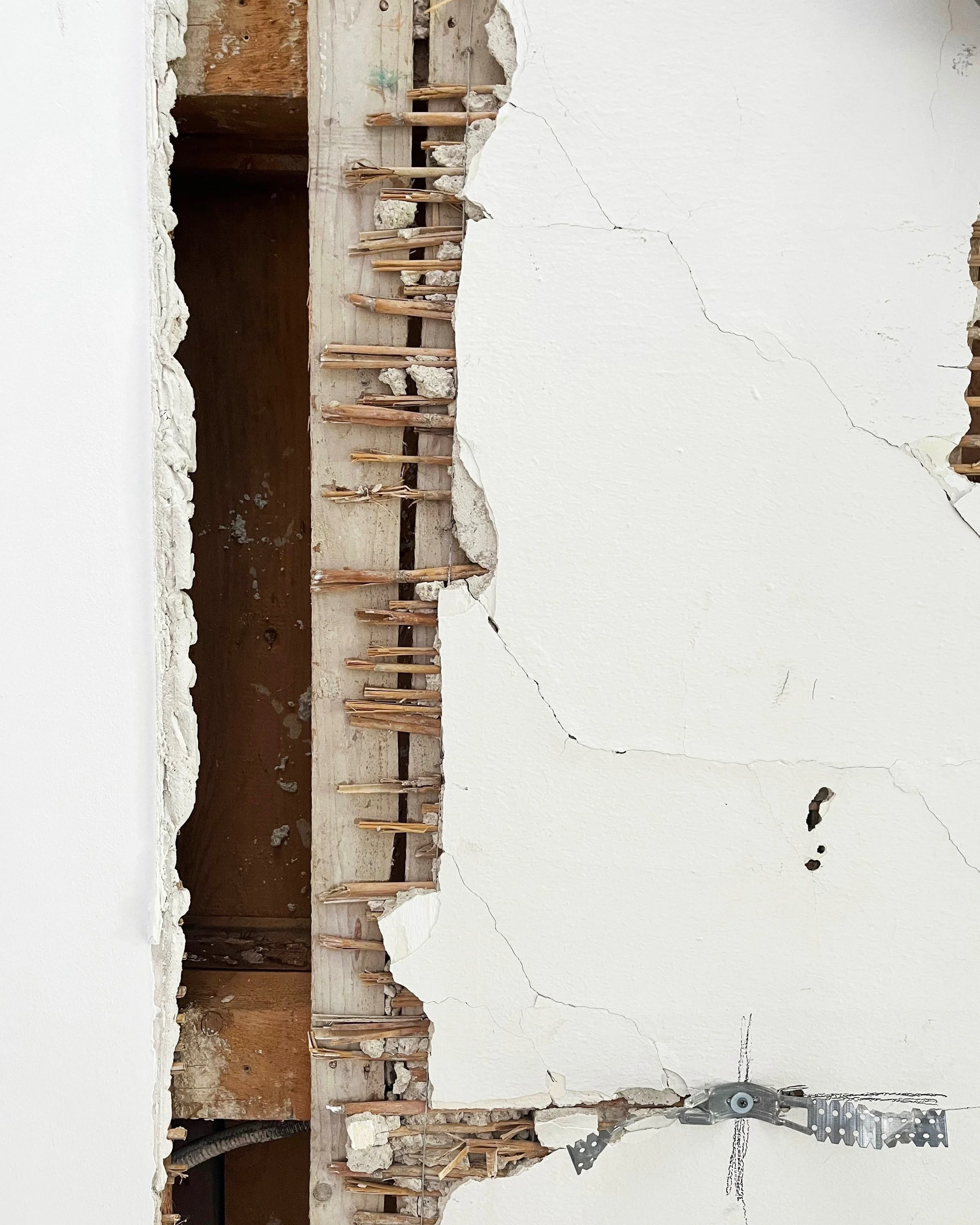 Detailaufnahme einer geöffneten Innenwand im Altbau vor der Sanierung mit freigelegter Schilfrohr-Putzträger-Konstruktion, Holzbalken und beschädigtem Gipsputz.