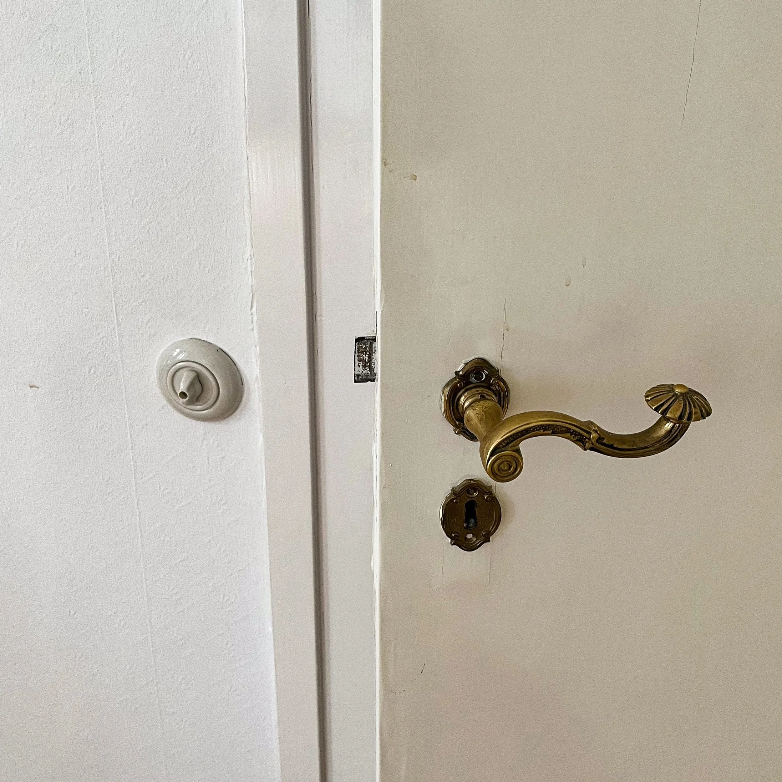 Detailaufnahme einer weißen Tür mit historischem, geschwungenem Messing-Türgriff und passendem Schlüsselschild.