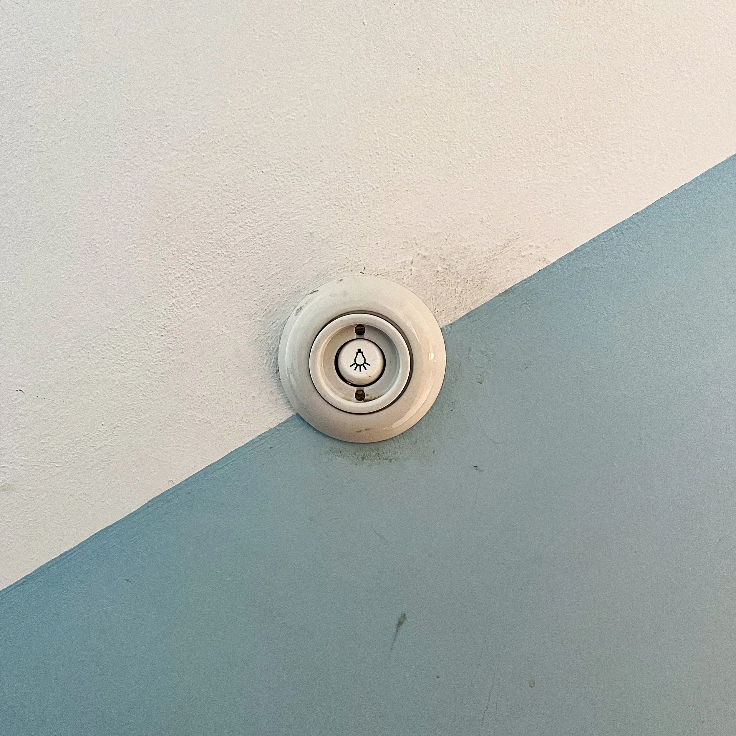 Detailaufnahme eines alten Lichtschalters auf einer zweifarbig gestrichenen Wand in Weiß und Hellblau.