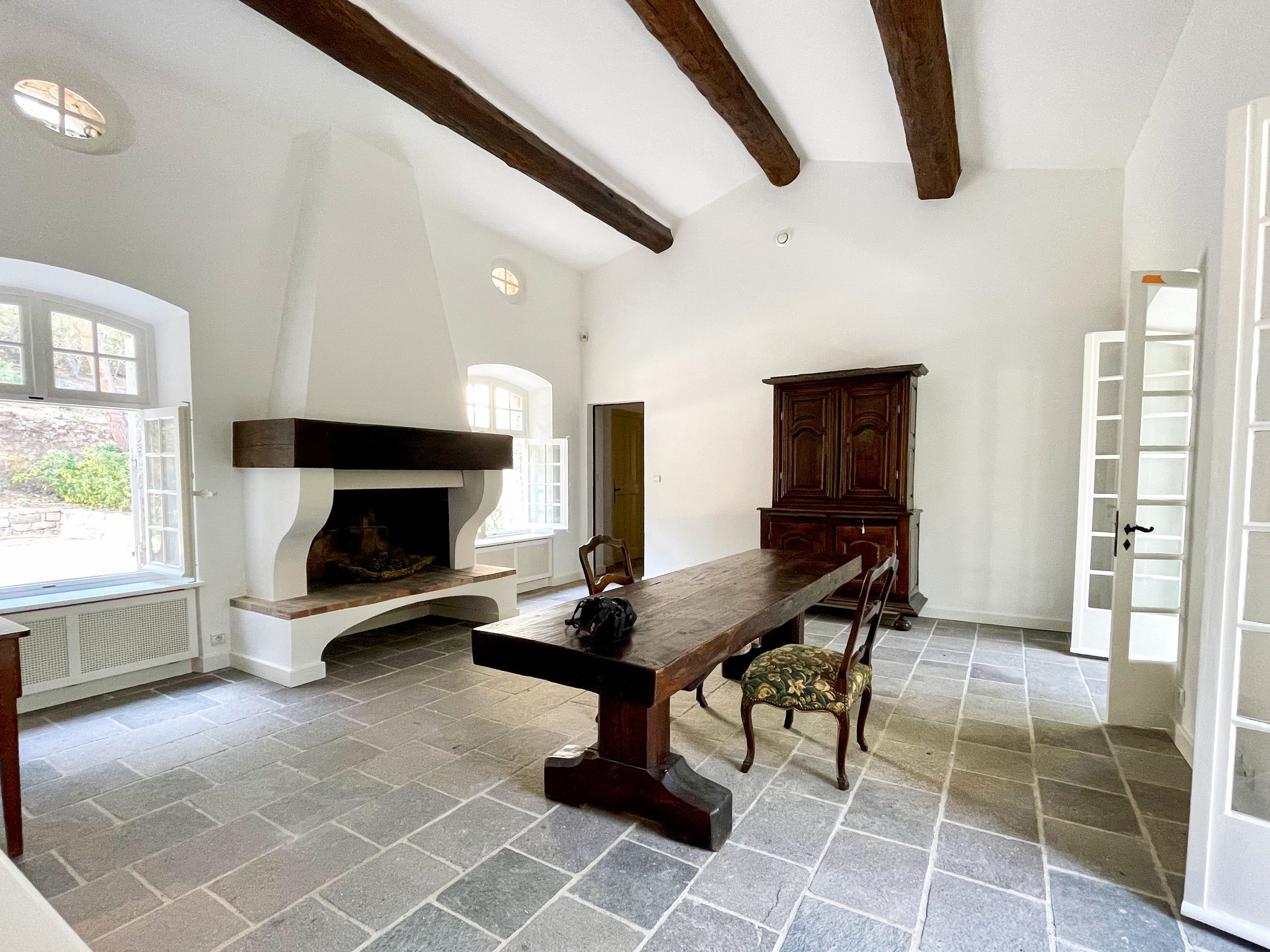 Großzügiger, helle interior gestalteter Essbereich im provenzalischen Stil mit freiliegenden Holzbalken an der Decke, großem Holz-Esstisch, Kamin und dunklem Steinboden.