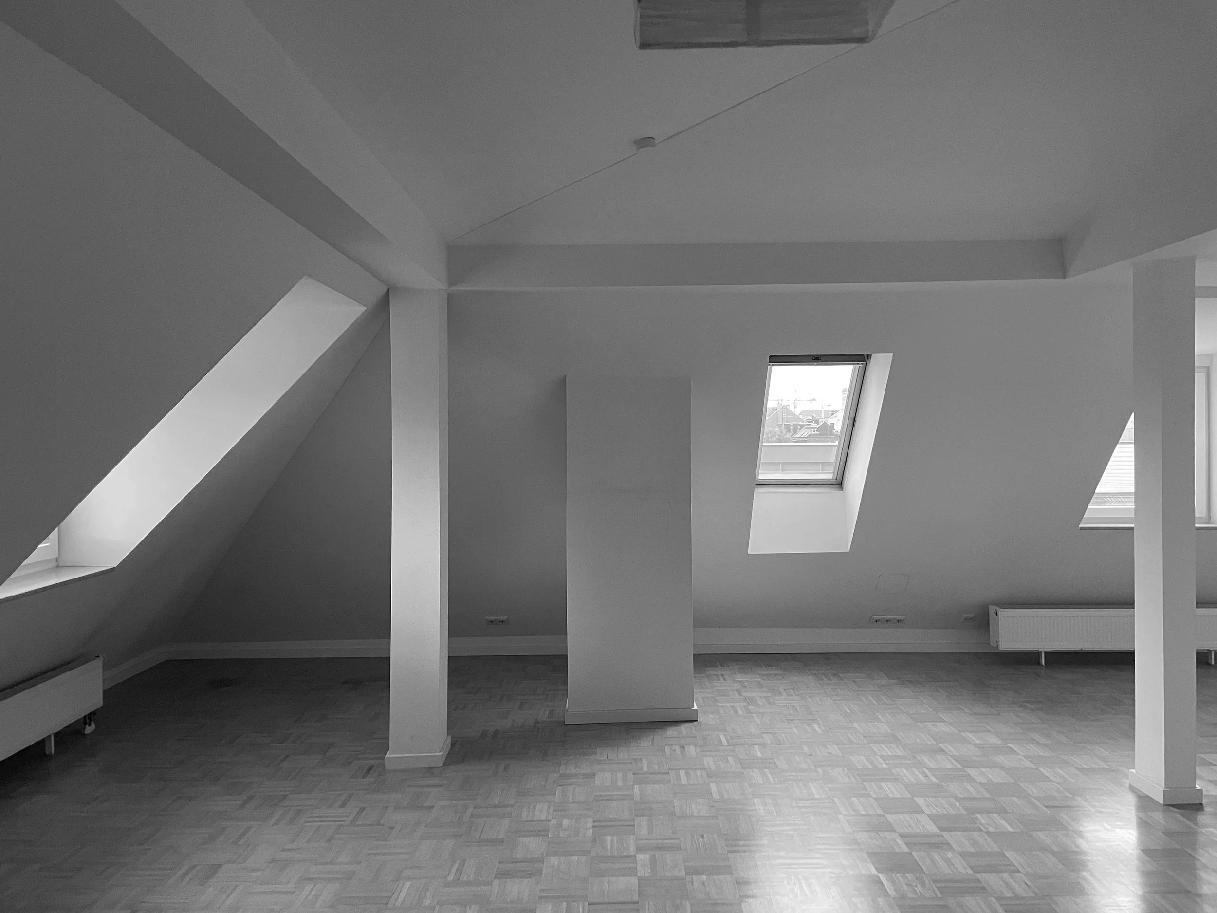Unmöblierter Dachgeschossraum vor der Sanierung mit sichtbaren Dachschrägen, weißen Wänden, mehreren Dachflächenfenstern und Parkettboden.