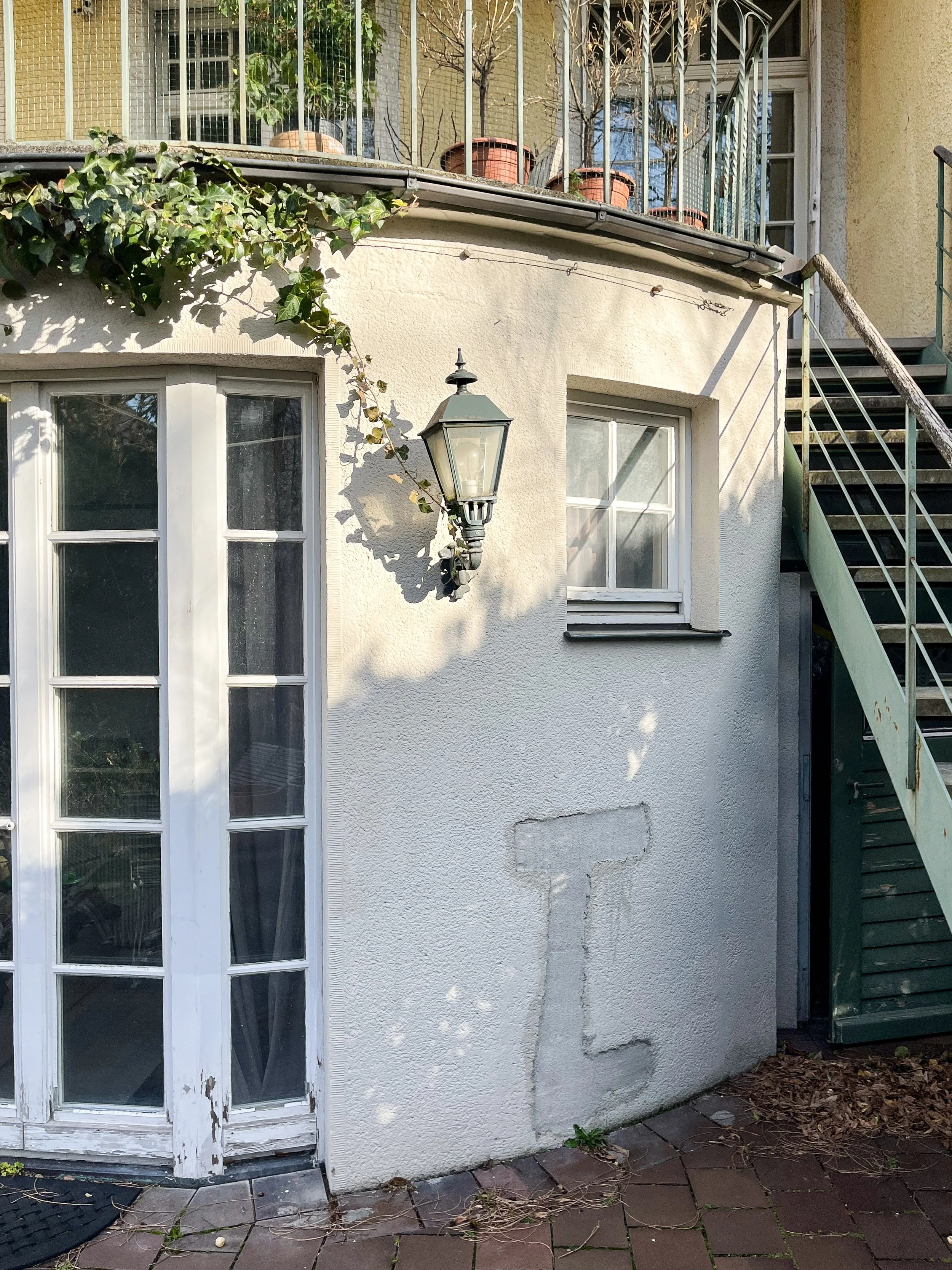 Außenaufnahme eines denkmalgeschützten Altbaus vor der Sanierung mit weißer Sprossentür, verputzter Fassade, Balkon und Stahltreppe.