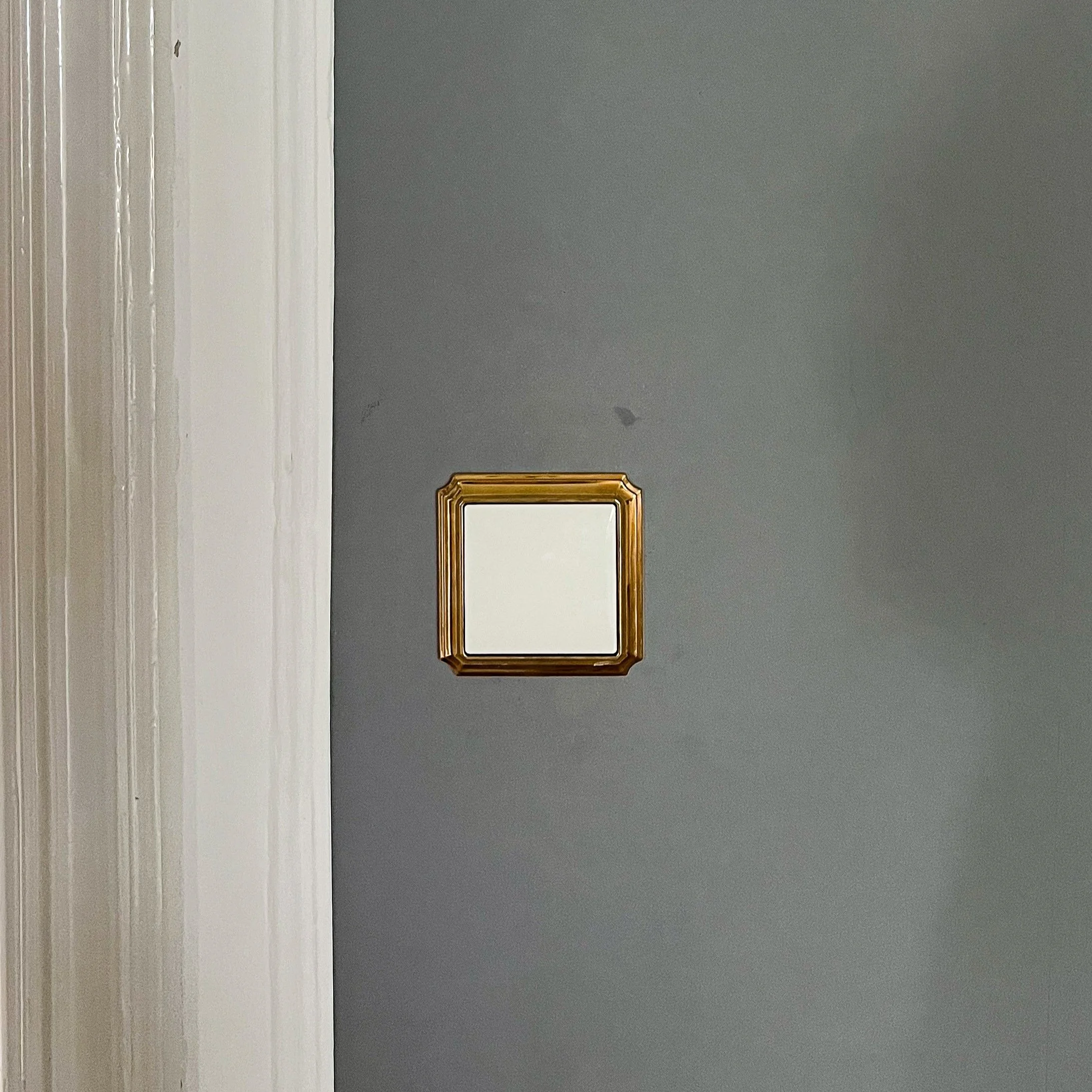 Detailaufnahme eines Lichtschalters mit einem Goldrahmen auf einer gestrichenen Wand in Dunkelgrau.