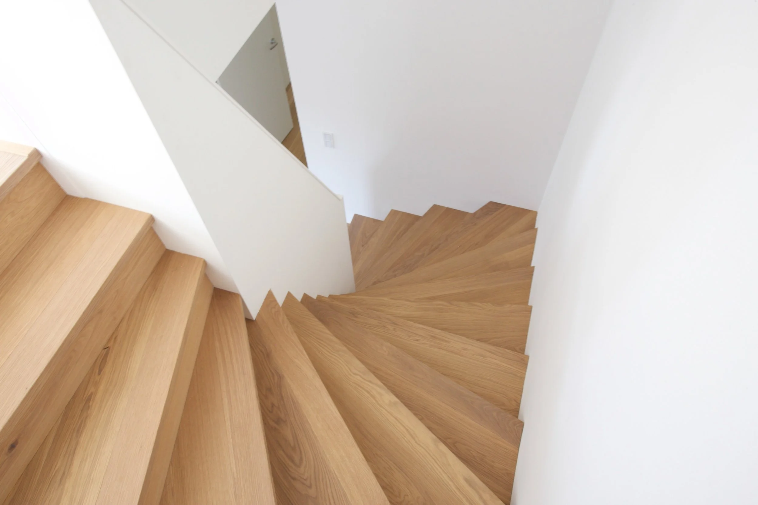 Das Eichenholz der minimalistischen Treppe fließt in den Bodenbelag fugenlos über.