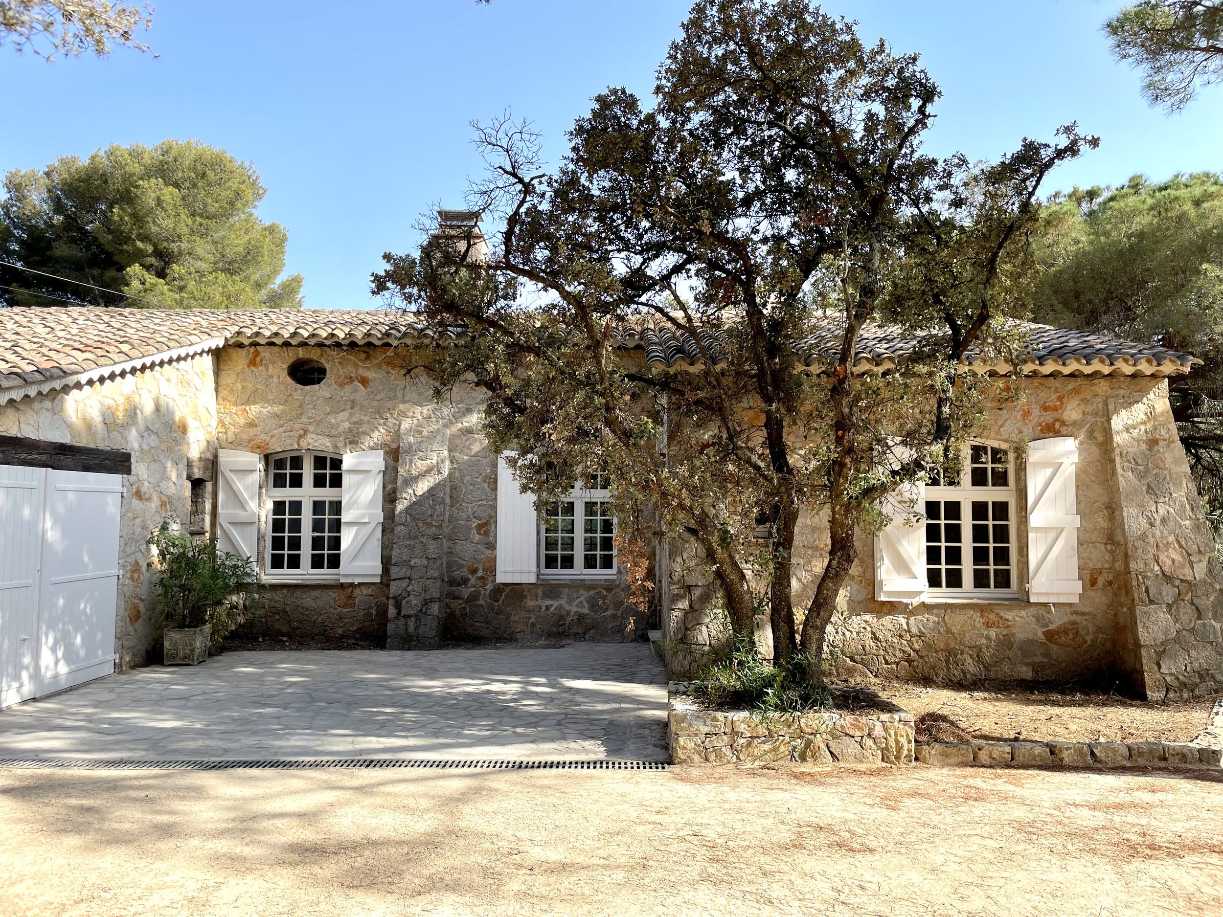 Eingeschossiges provenzalisches Sommerhaus in St. Tropez mit Natursteinmauerwerk, weiß gestrichenen Holz-Klappläden, Ziegeldach und Schatten spendendem Pinienbaum im Hof.