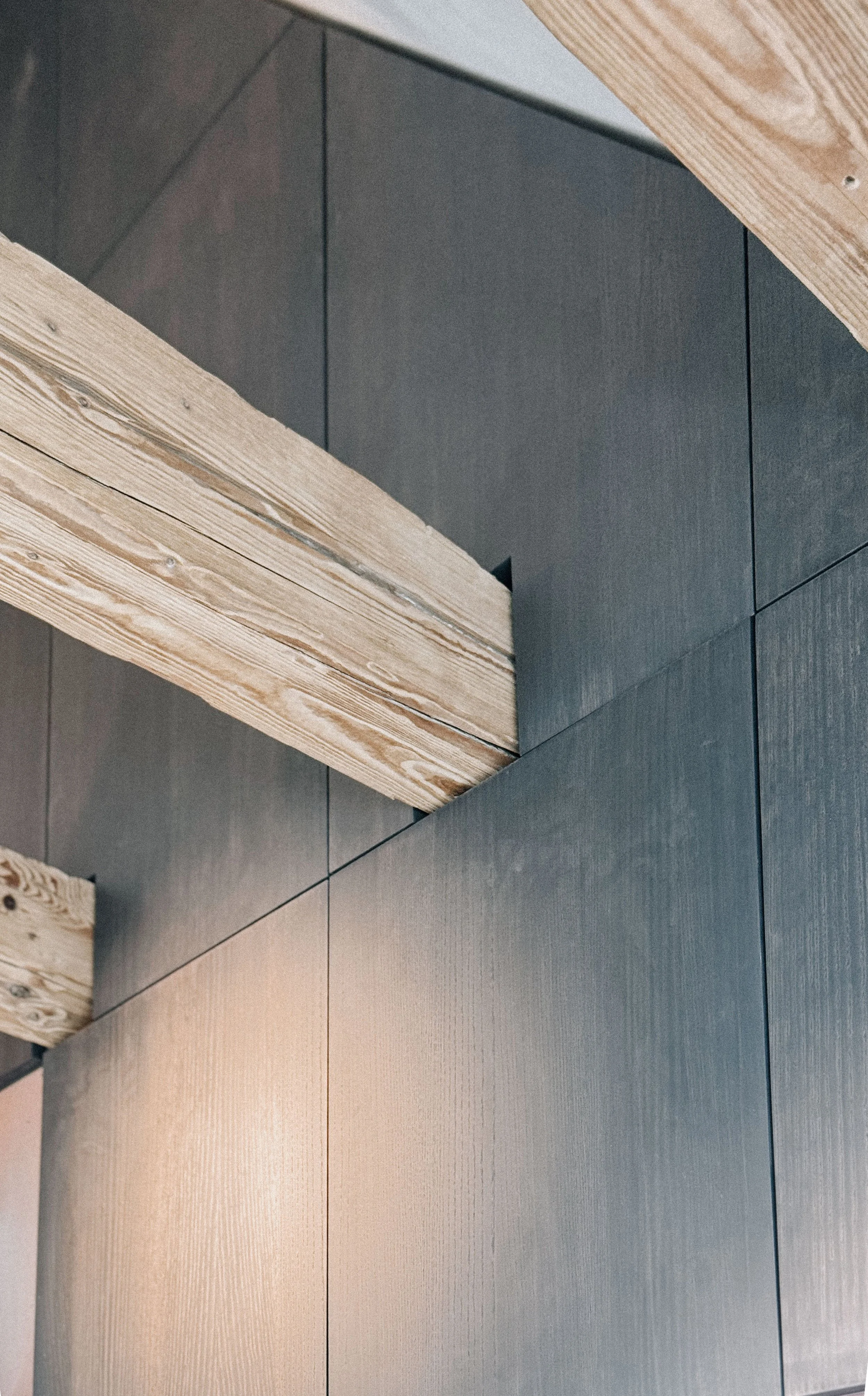 Nahaufnahme eines freiliegenden Holzbalkens, der präzise in eine dunkelgrau gebeizte Wandverkleidung aus Holz im modernen Innenausbau eingepasst ist.